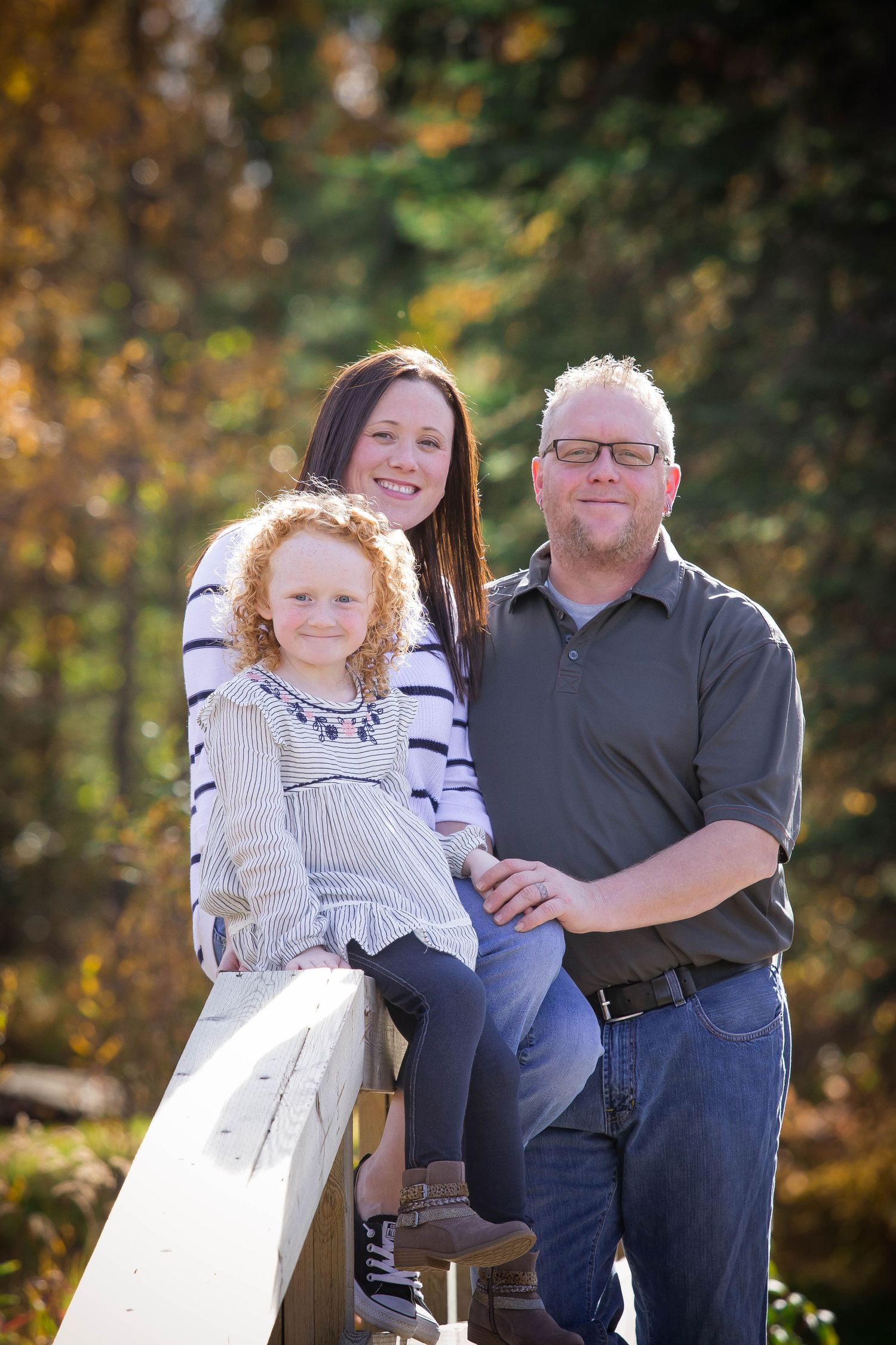Outdoor family photo session on wooden bench surrounded by autumn trees.