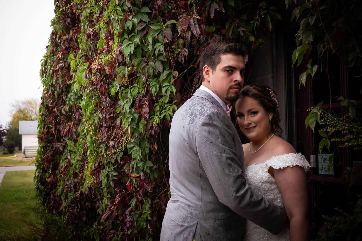 Romantic couple poses against vine-covered wall in elegant wedding attire.