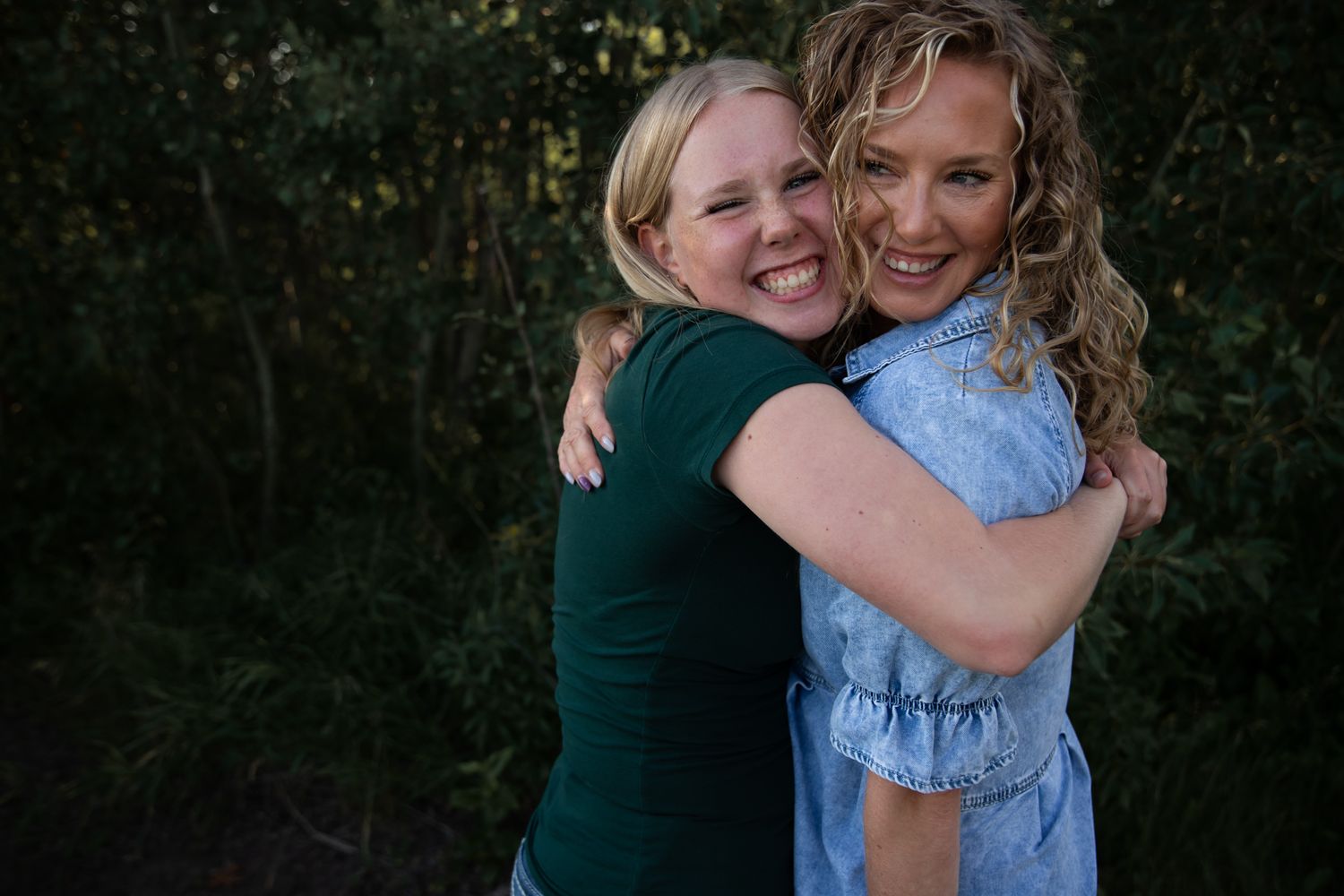 Two people share a warm hug while laughing outdoors during a photo session.