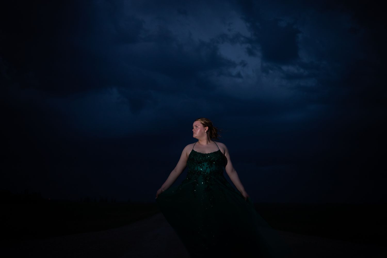 A silhouette in an elegant gown poses against a moody night sky.