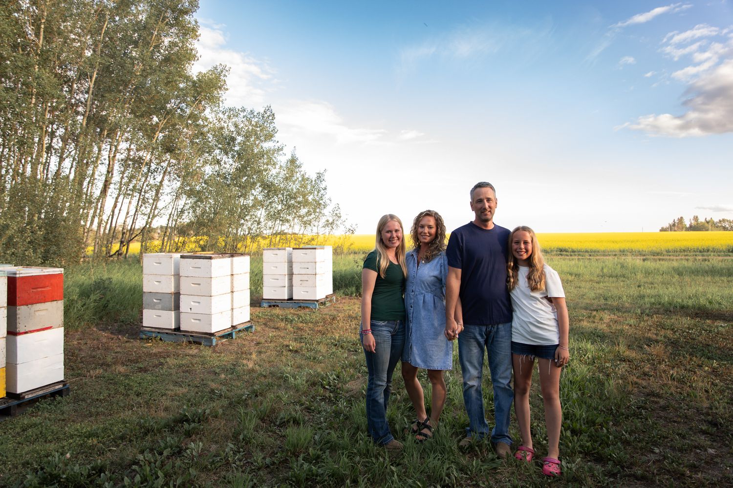 Family portrait taken near beehives with a bright yellow canola field in the background.