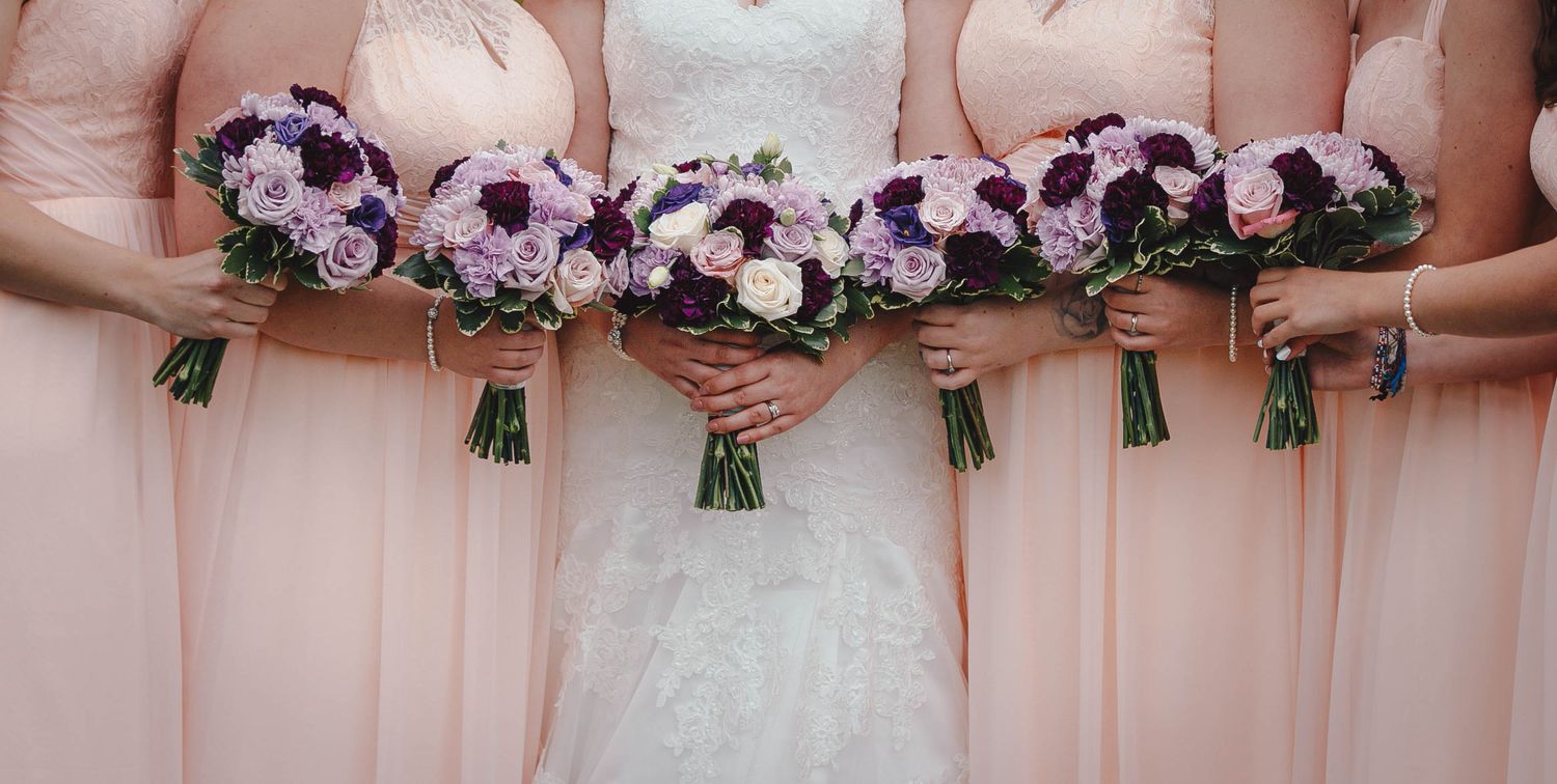 Purple and pink wedding bouquets held against pink bridesmaid dresses.