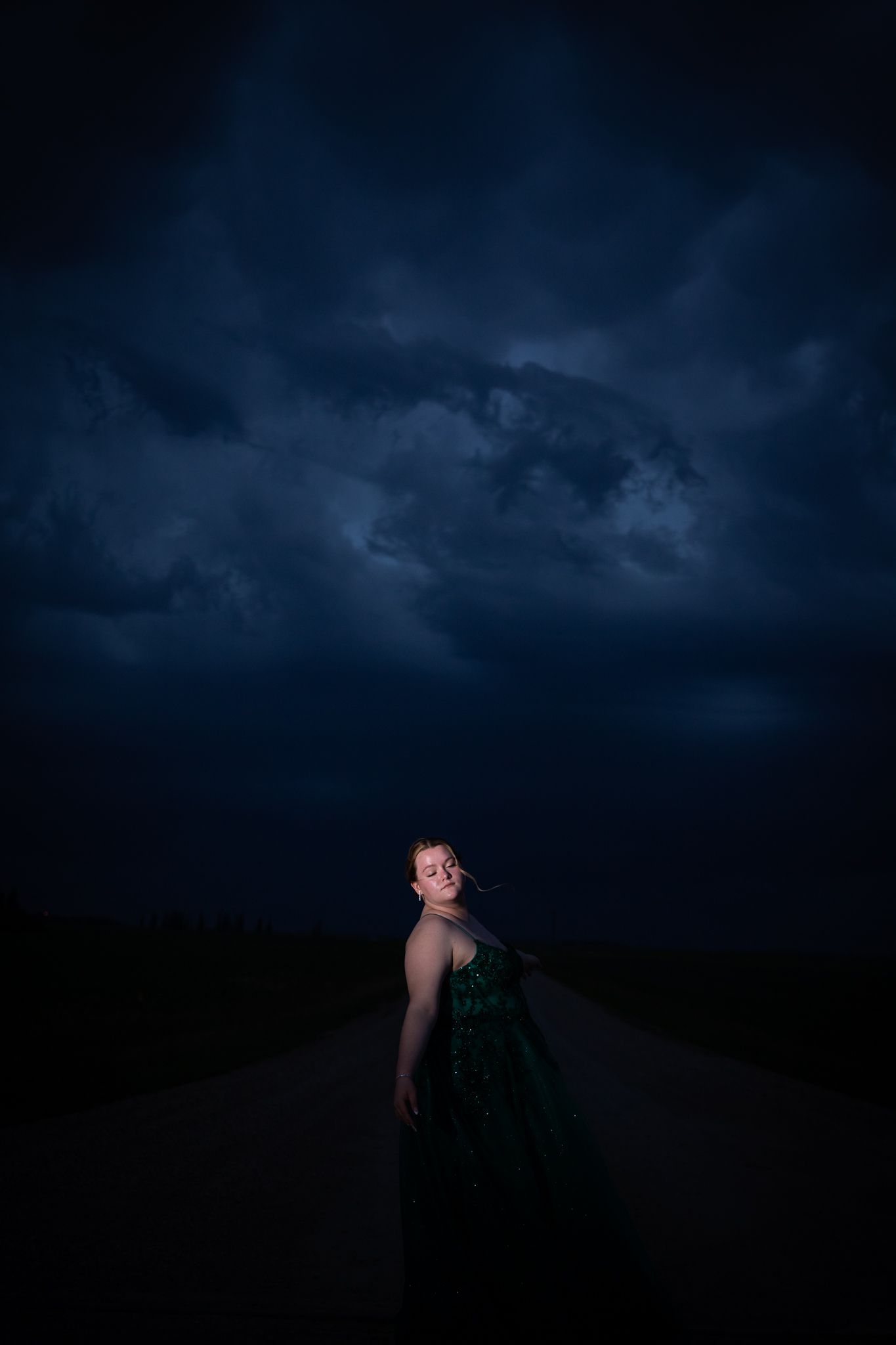 A dramatic nighttime portrait shows a figure in a dark green gown against stormy skies.