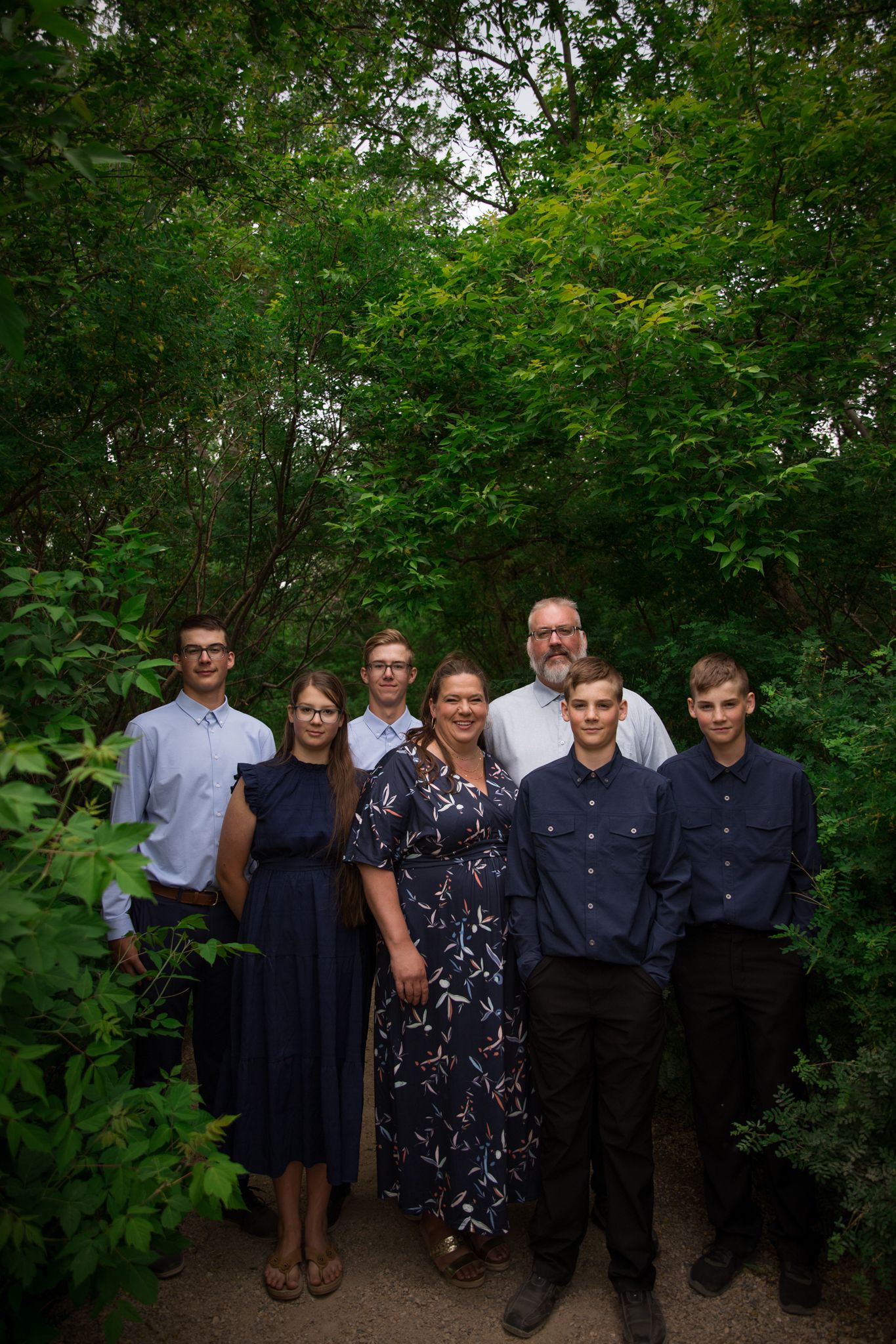 Group photo of formally dressed people standing together in a wooded outdoor setting.