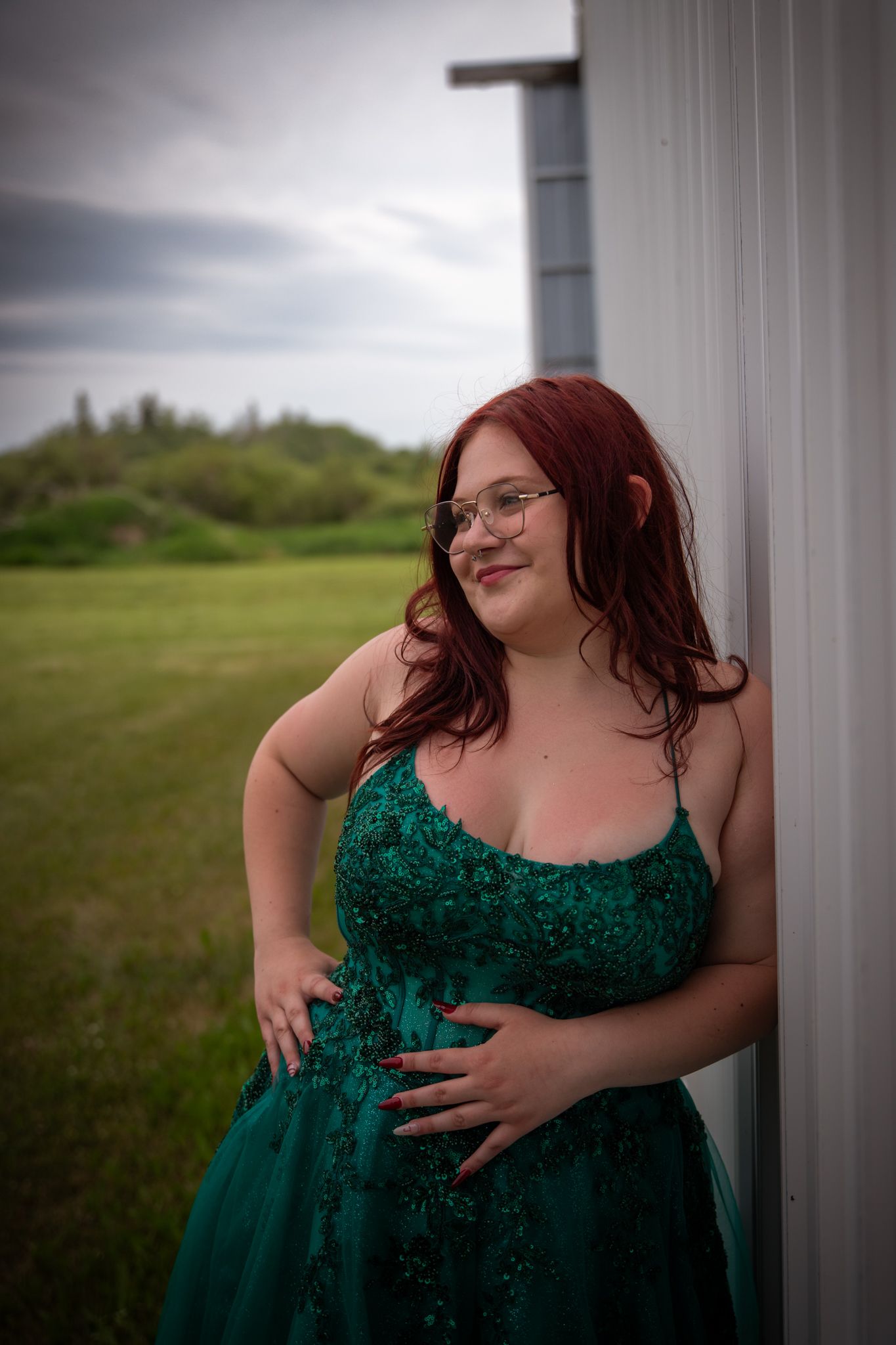 Elegant poses in emerald formal gown against white industrial backdrop.