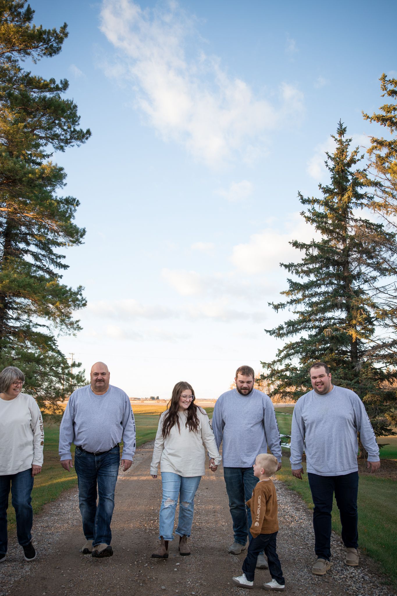 Group walking casually along a path with evergreen trees and blue sky backdrop.
