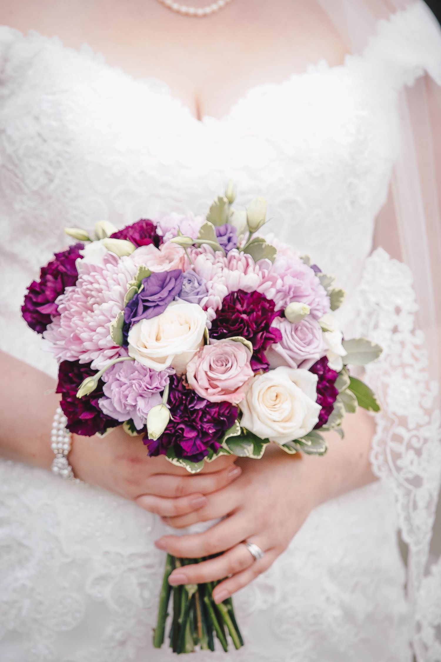 A stunning bridal bouquet featuring pink roses, purple carnations, and white flowers.