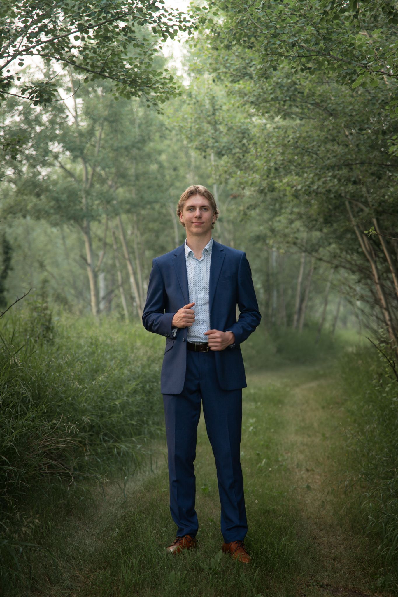 A scenic portrait shot on a tree-lined dirt path with natural greenery in the background.