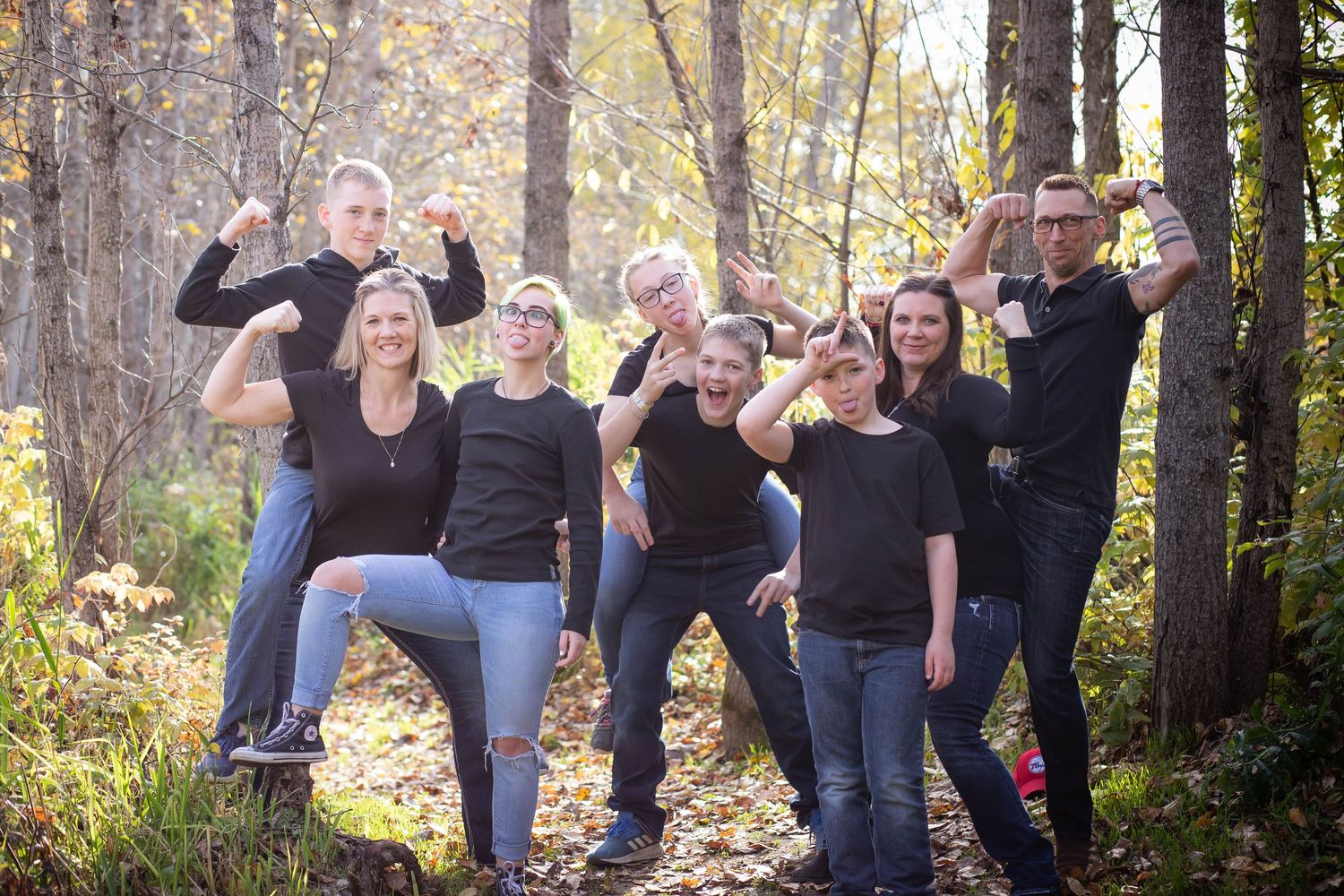 A playful group strikes fun poses while standing together in a sunlit forest.