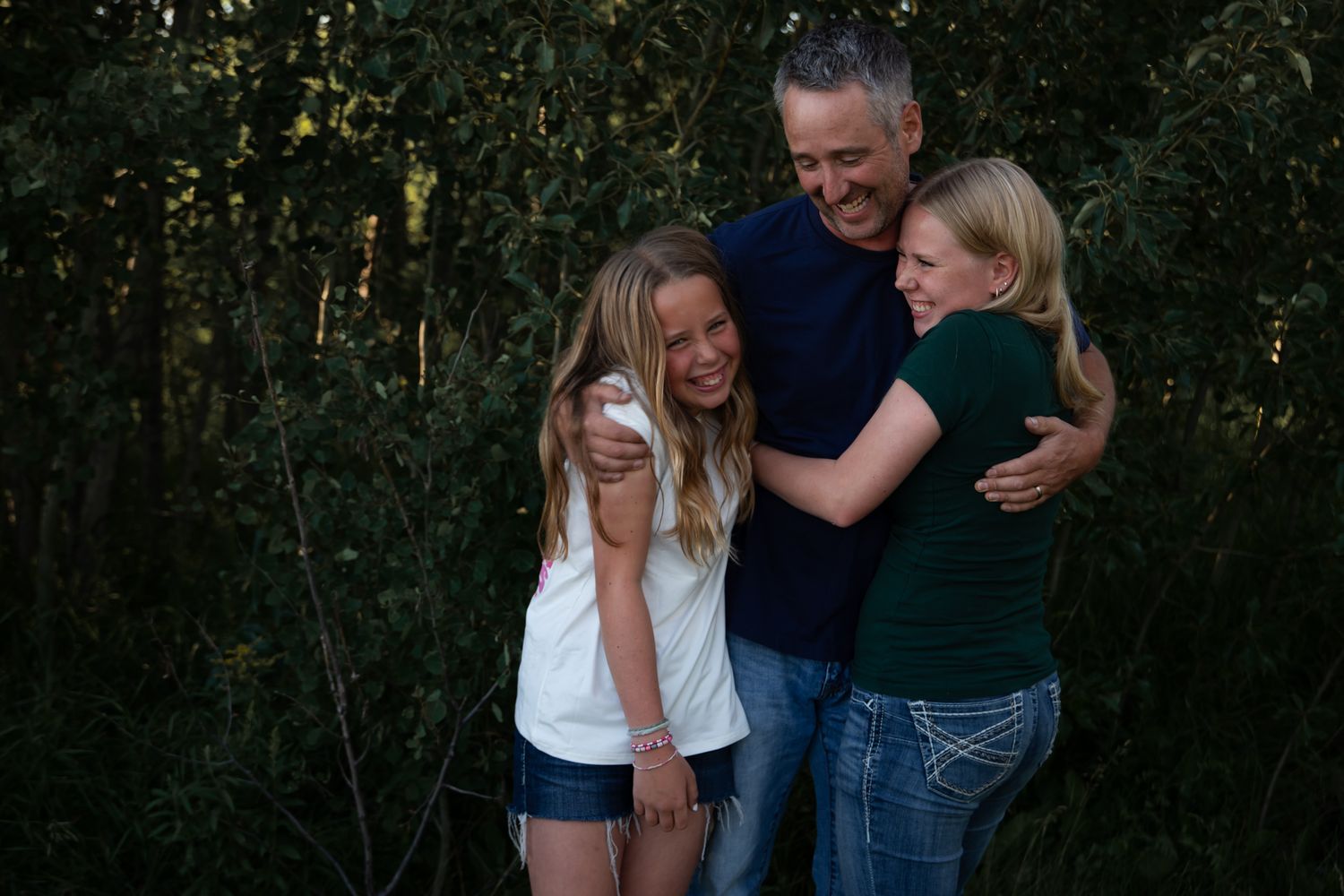 A group shares laughter and hugs together against a wooded background at dusk.