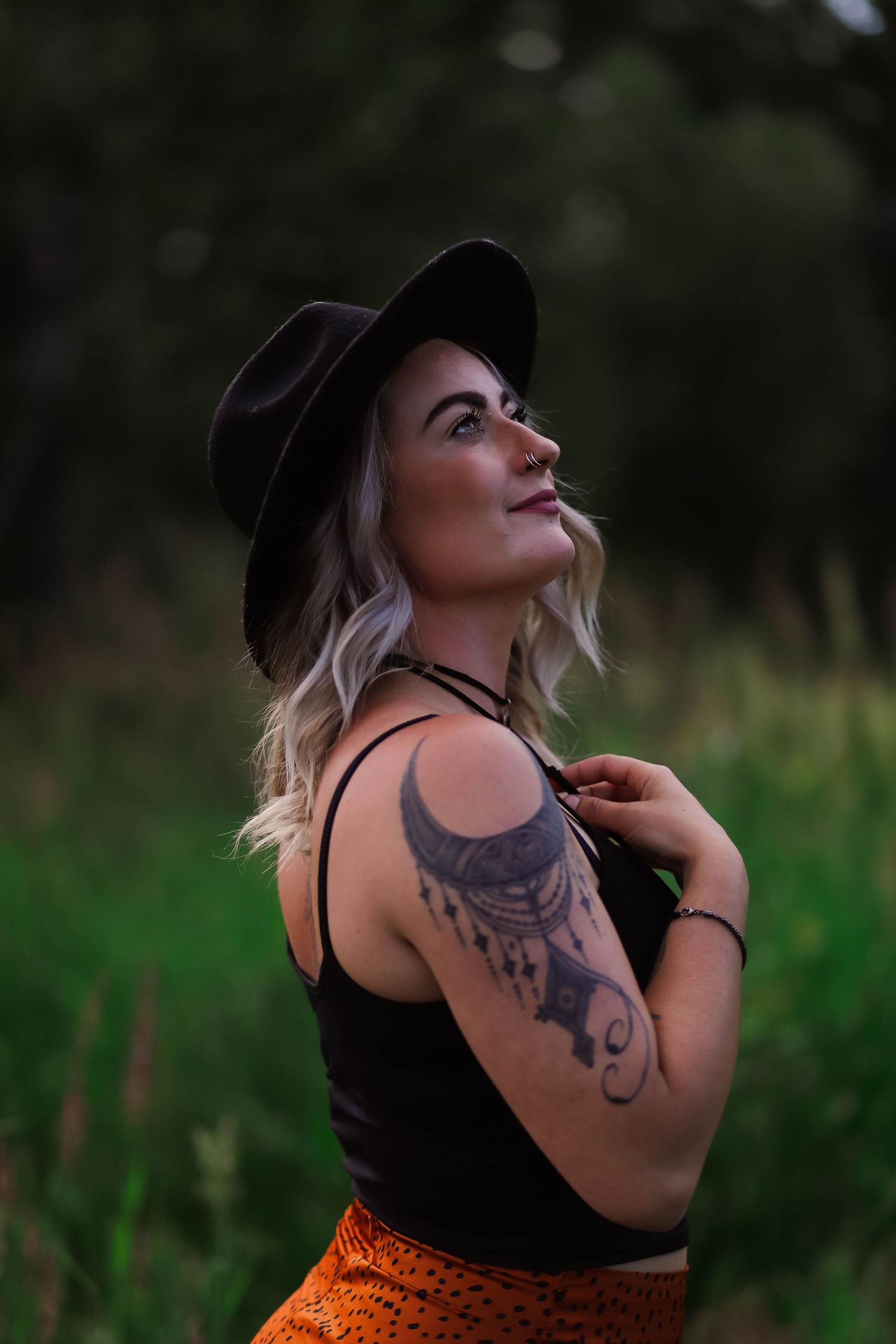 Artistic outdoor portraits featuring tattoos and black hat against green foliage.