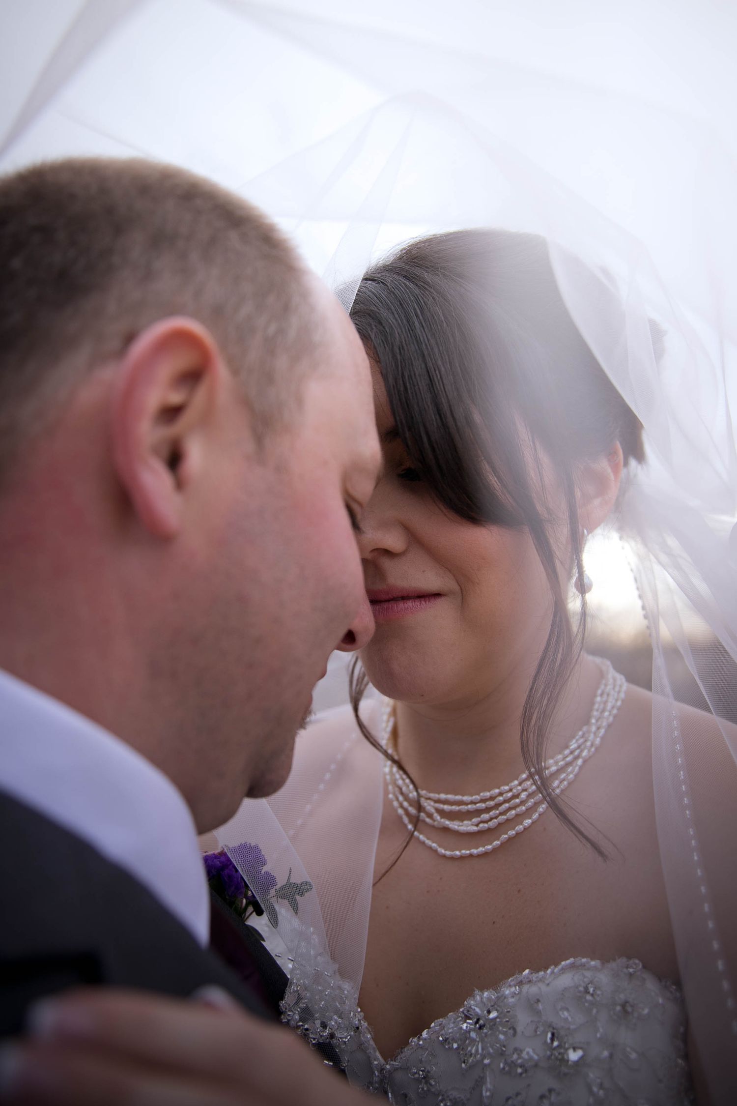 Intimate moment between newlyweds sharing a tender moment under bridal veil.