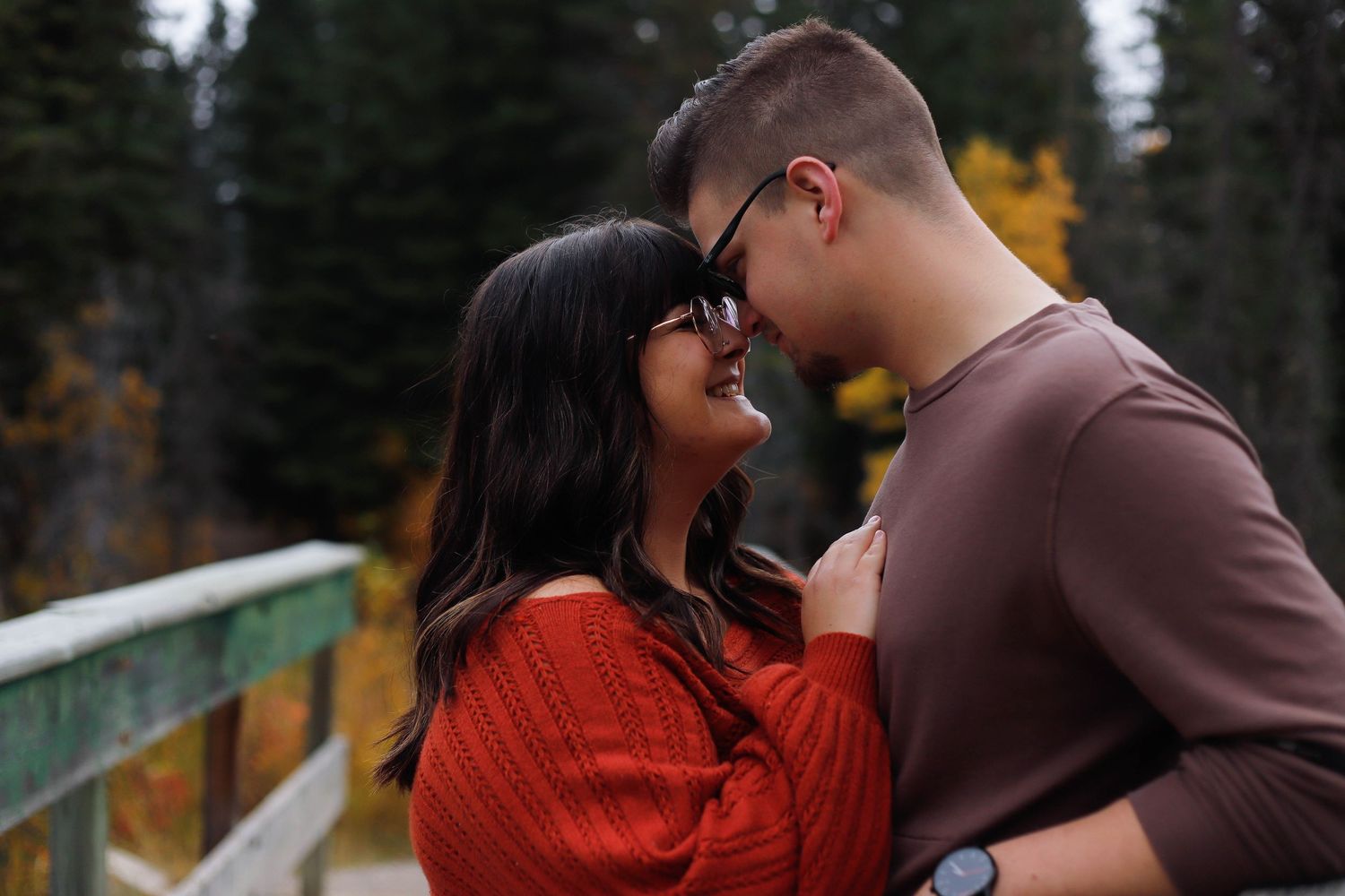 A couple shares a tender moment on a bridge surrounded by autumn trees and golden light.