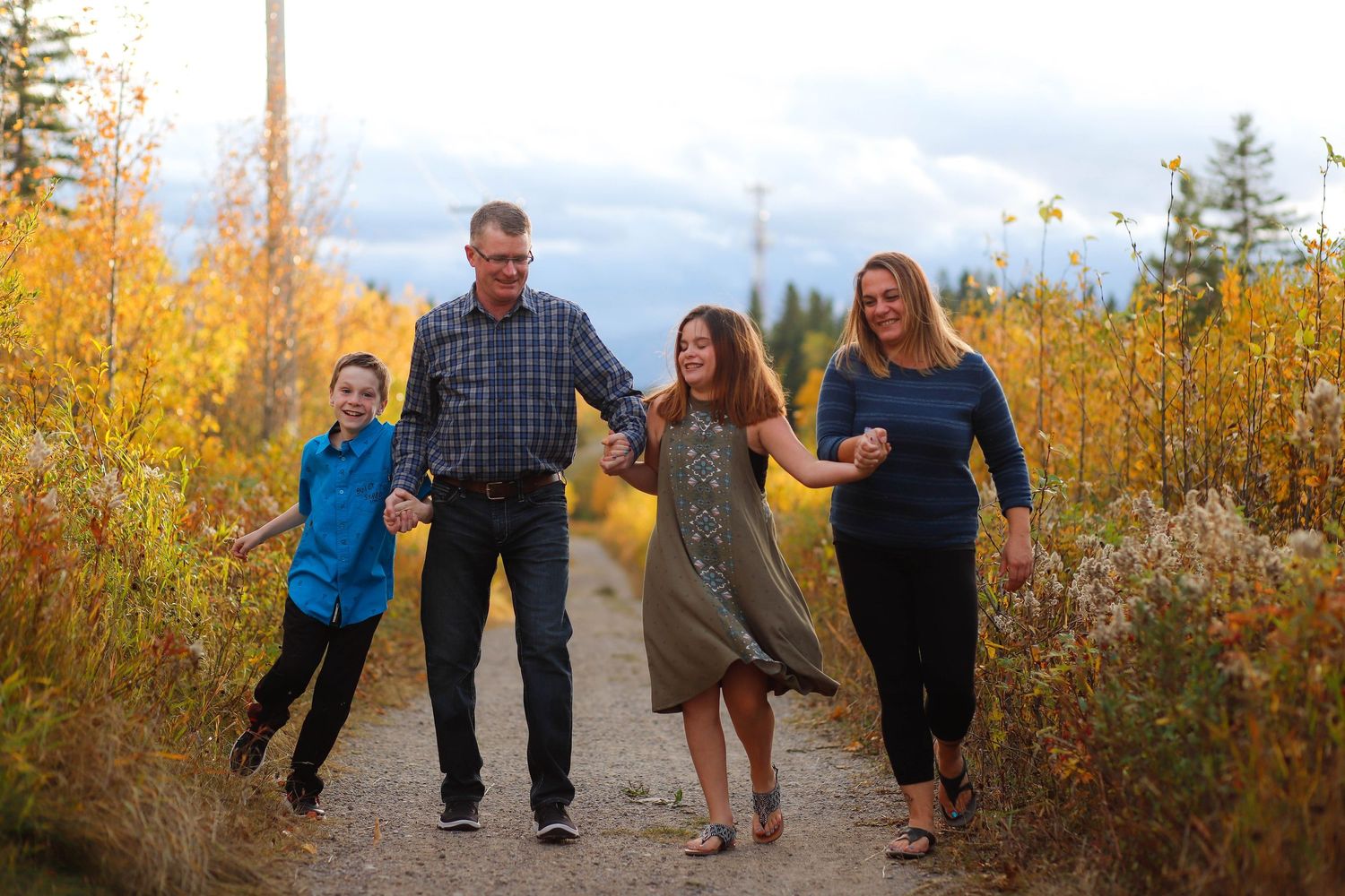 Family walking together through autumn foliage with golden light filtering through trees.