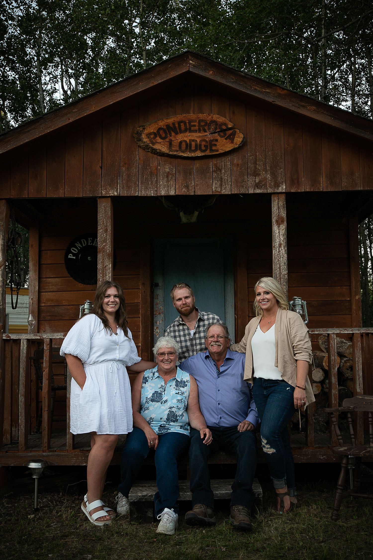 A group poses on the porch of Wonderbay Lodge, a rustic wooden cabin in the woods.
