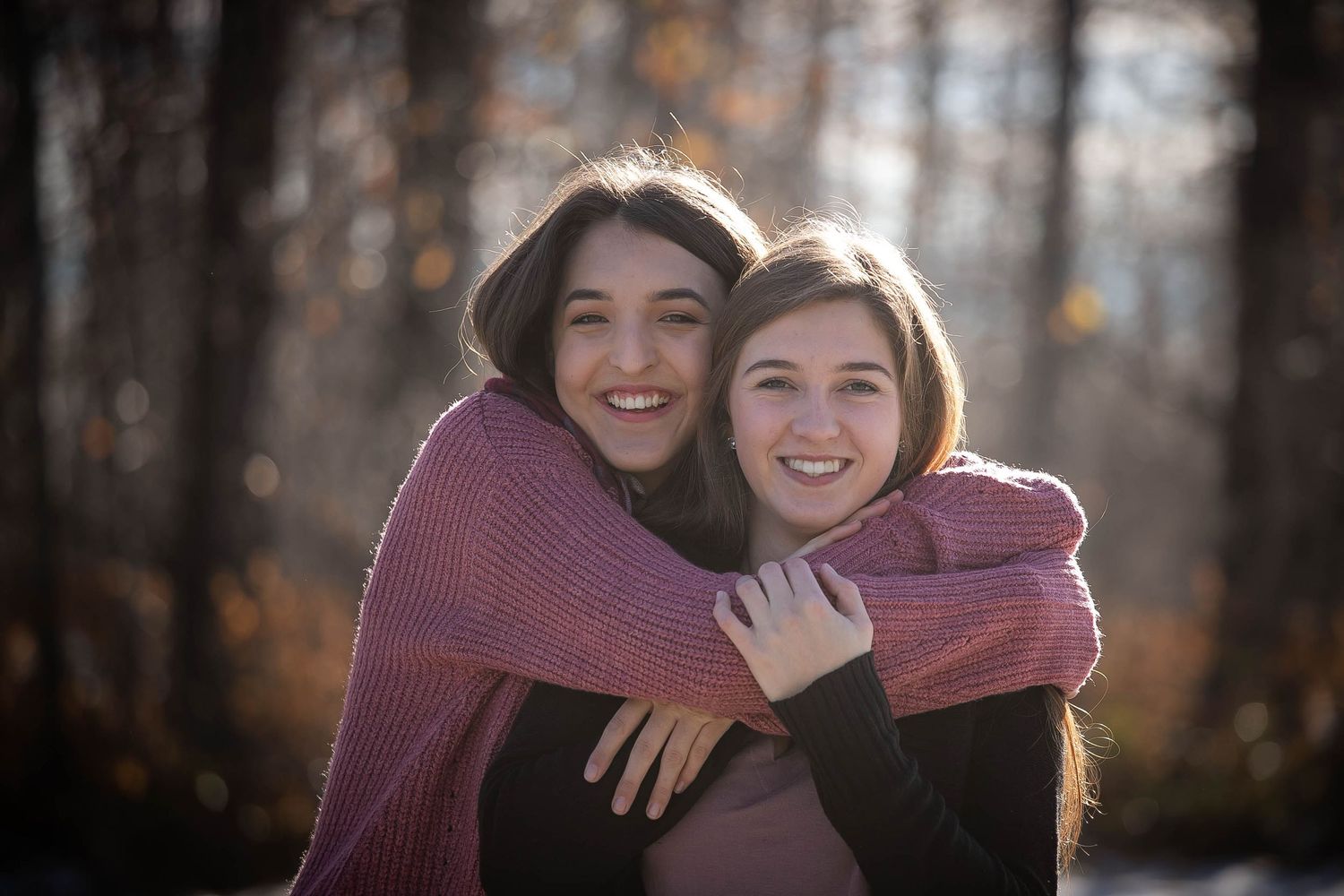 Two people sharing a warm embrace while wearing cozy sweaters in an autumn forest setting.