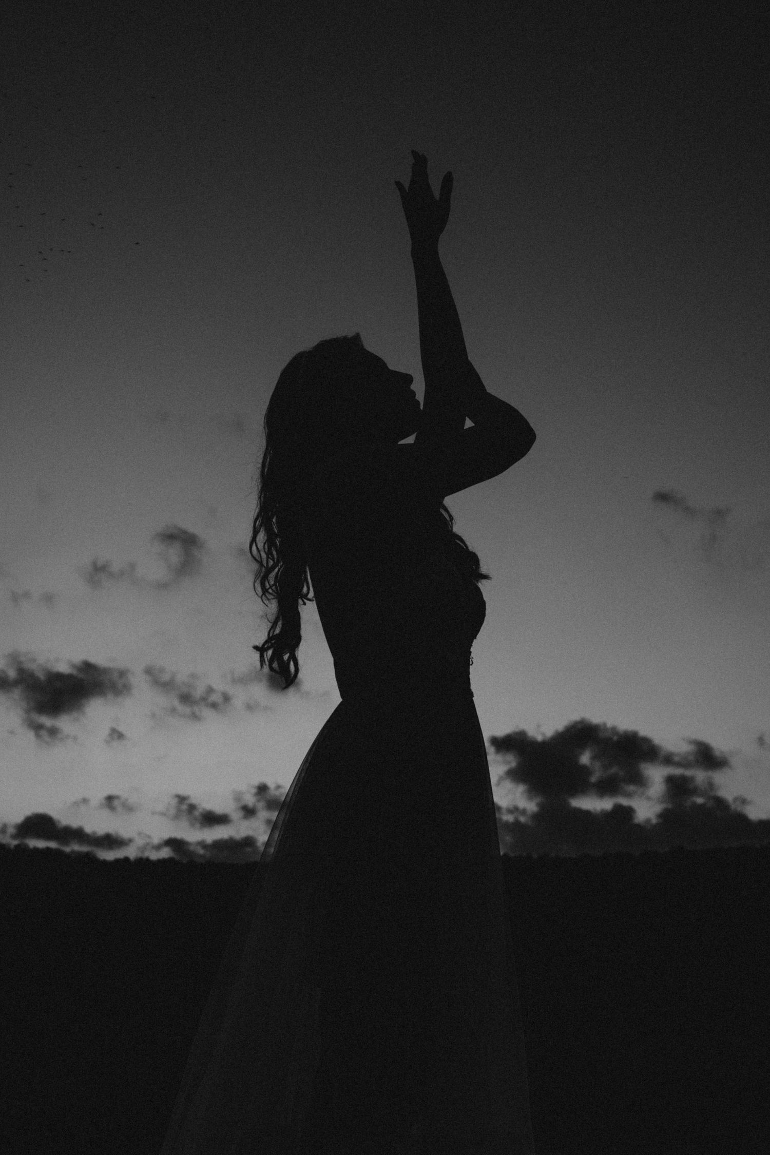 Black and white portrait photo of a woman at a park reaching out to the sky for a more cinematic style of photography