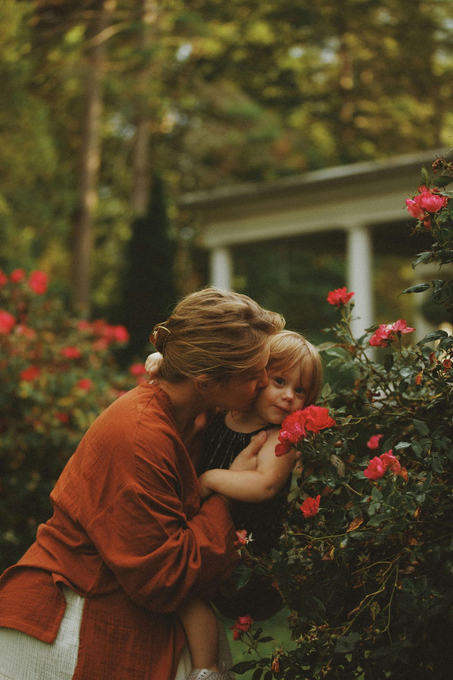 Mother and daughter portrait next to floral bushes outside home
