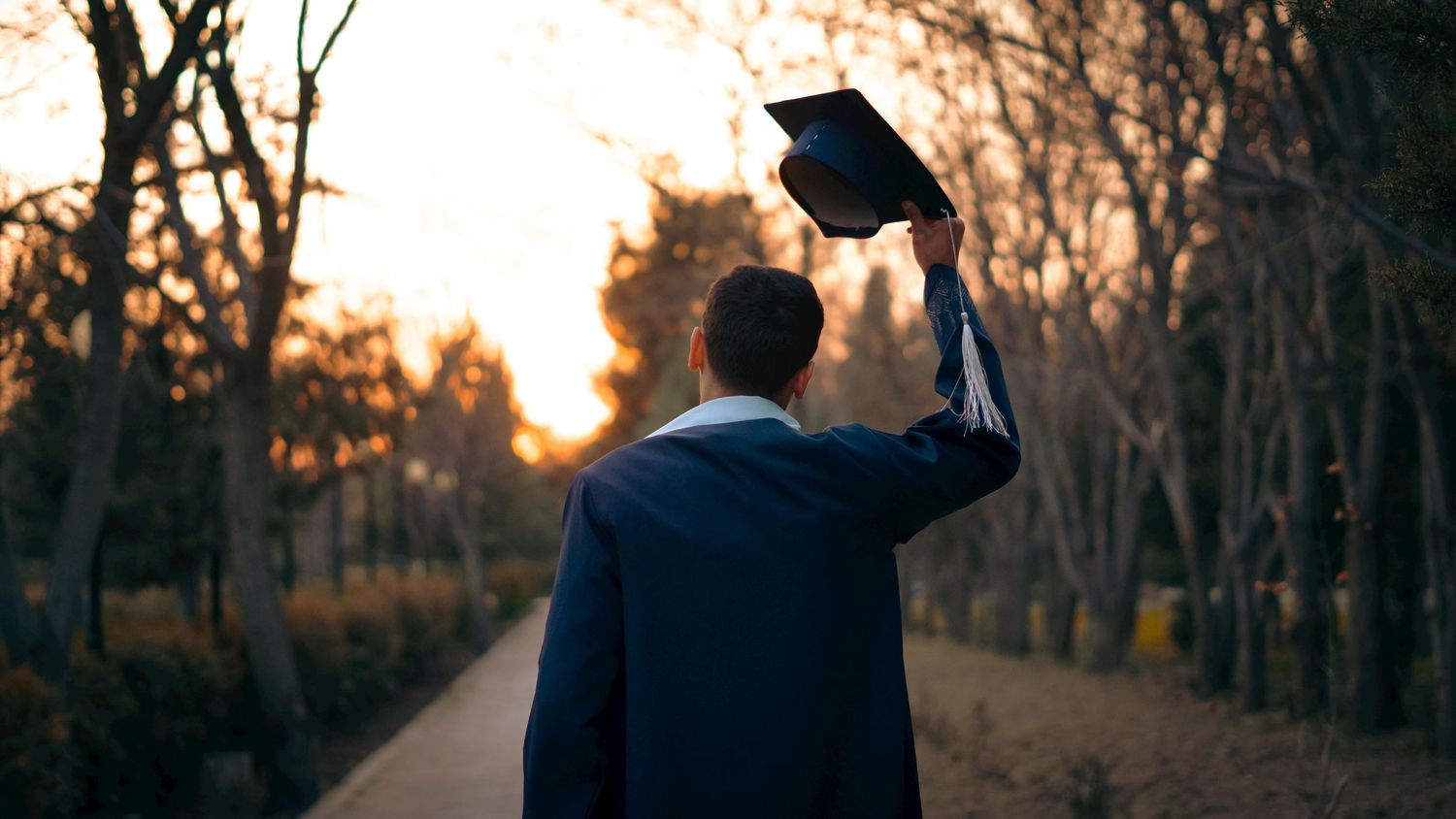 A graduation senior lifting his cap to the sky in enjoyment of achieving his graduation