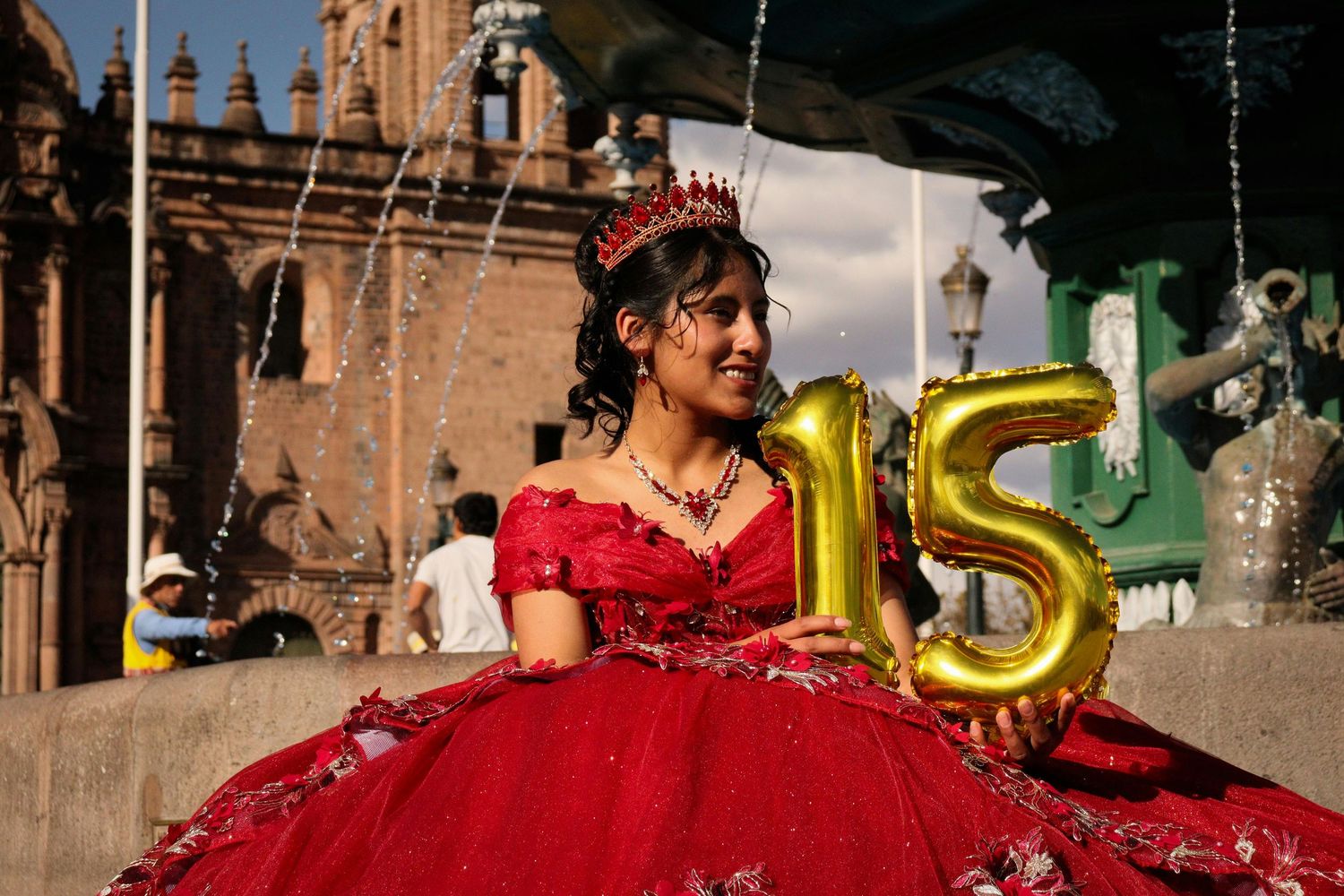 Quinceañera in a red dress with golden balloons in small town posing for photo