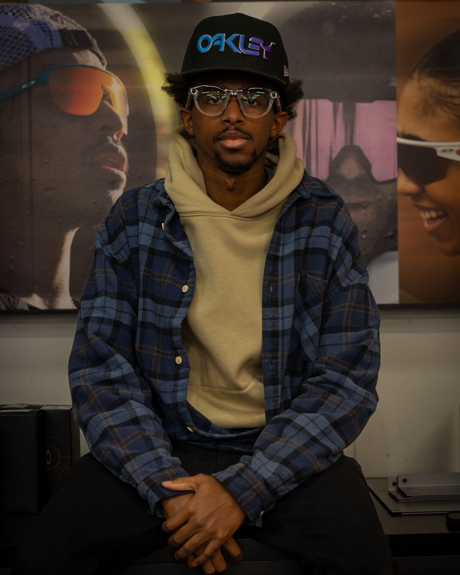Fashion candid portrait of a man seated indoors wearing layered street wear with artwork in the background