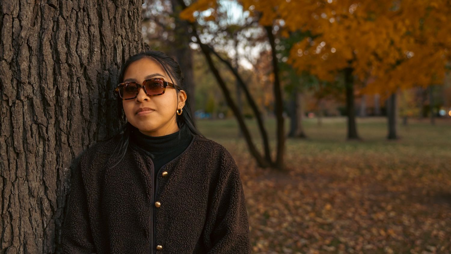 Park outdoor portrait of a woman leaning on a tree during autumn with warm natural light tones