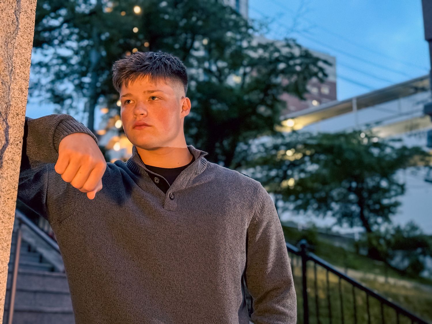 Outdoor portrait photography of a man leaning against a wall during blue hour with soft city lighting