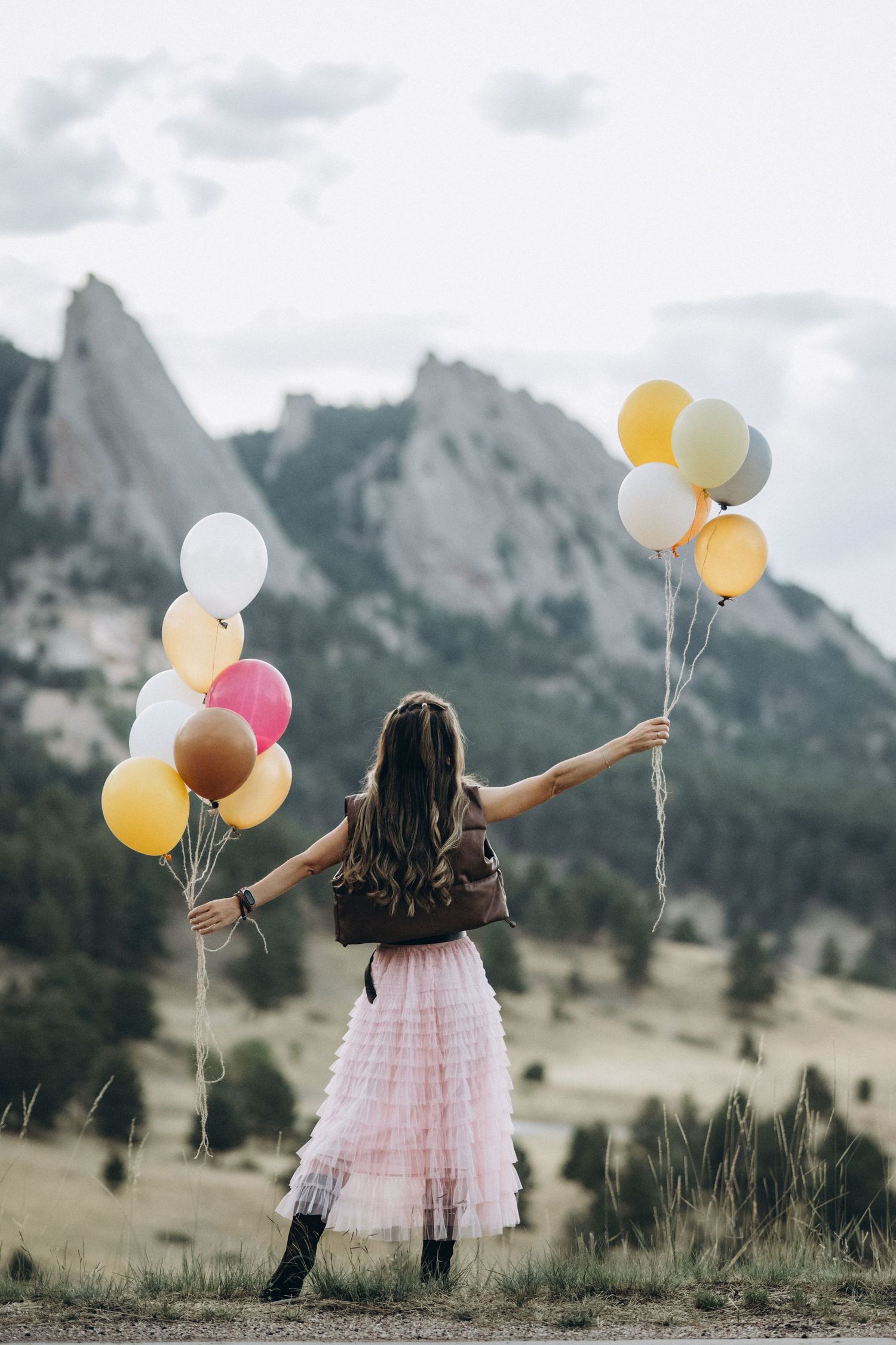 Girl in pink tulle skirt holding balloons facing the mountains, Boulder family photographer at NCAR, Colorado