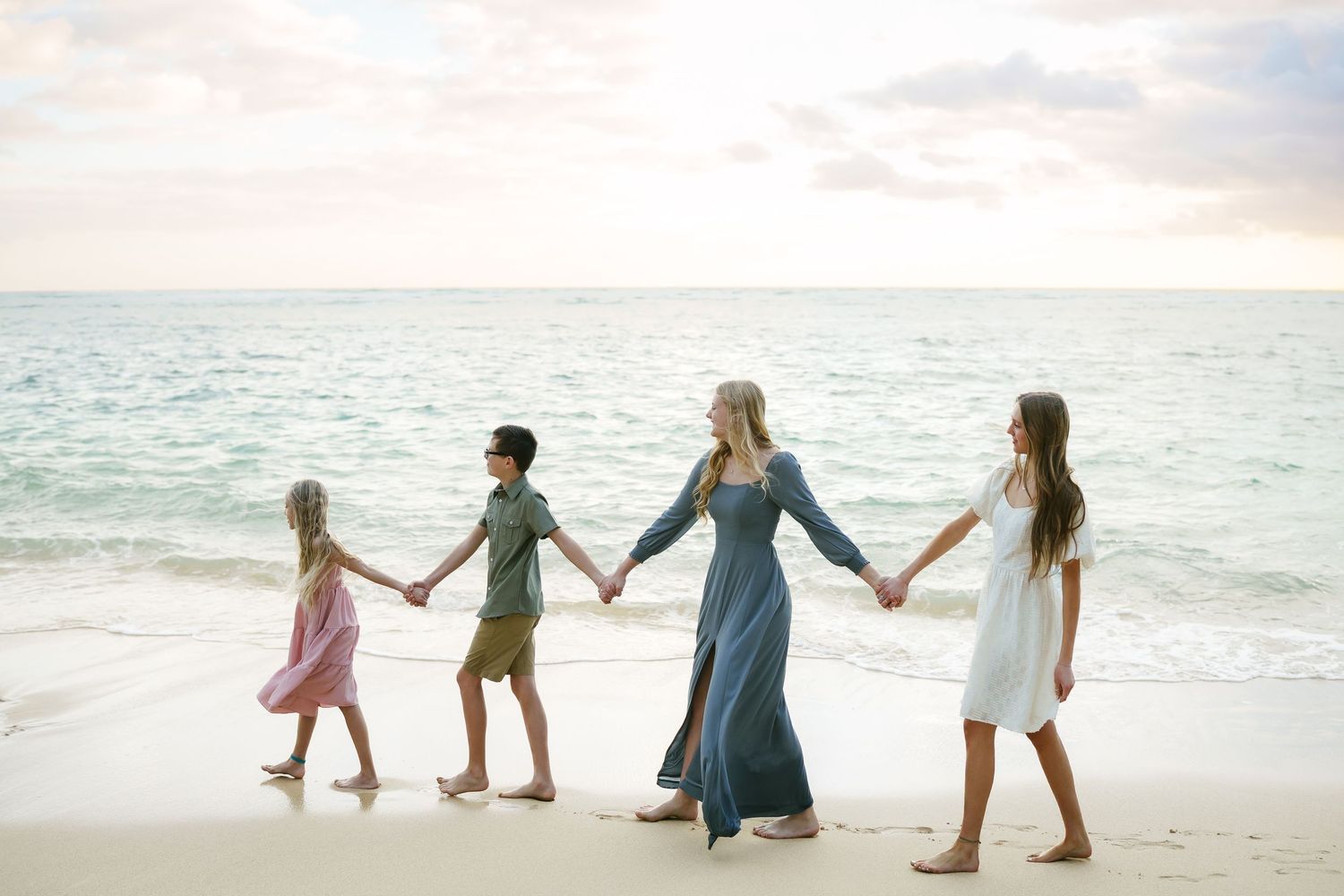A group holds hands while walking along a Kaaawa  beach at sunrise with turquoise waters in the background.