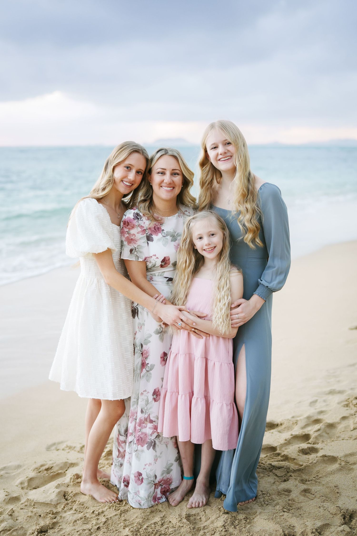 A mother with her three daughters in beautiful dresses at Ka’a’awa Beach, Oahu. A joyful family moment at sunrise with the ocean behind.