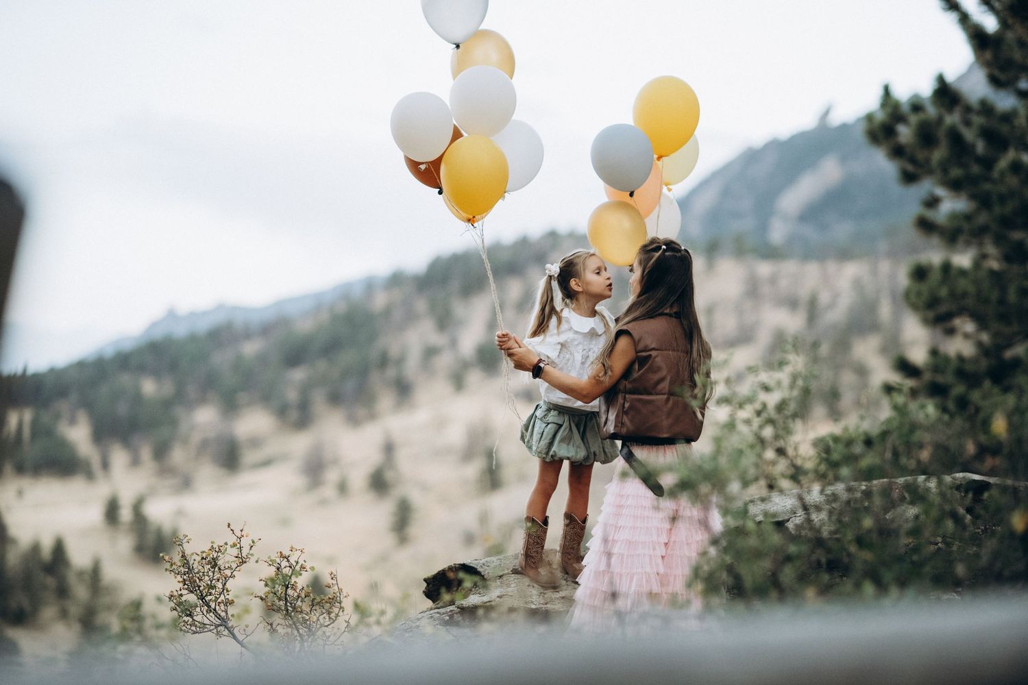 Mother and daughter with balloons in a wide mountain meadow, Flatirons behind, NCAR Boulder family photo session