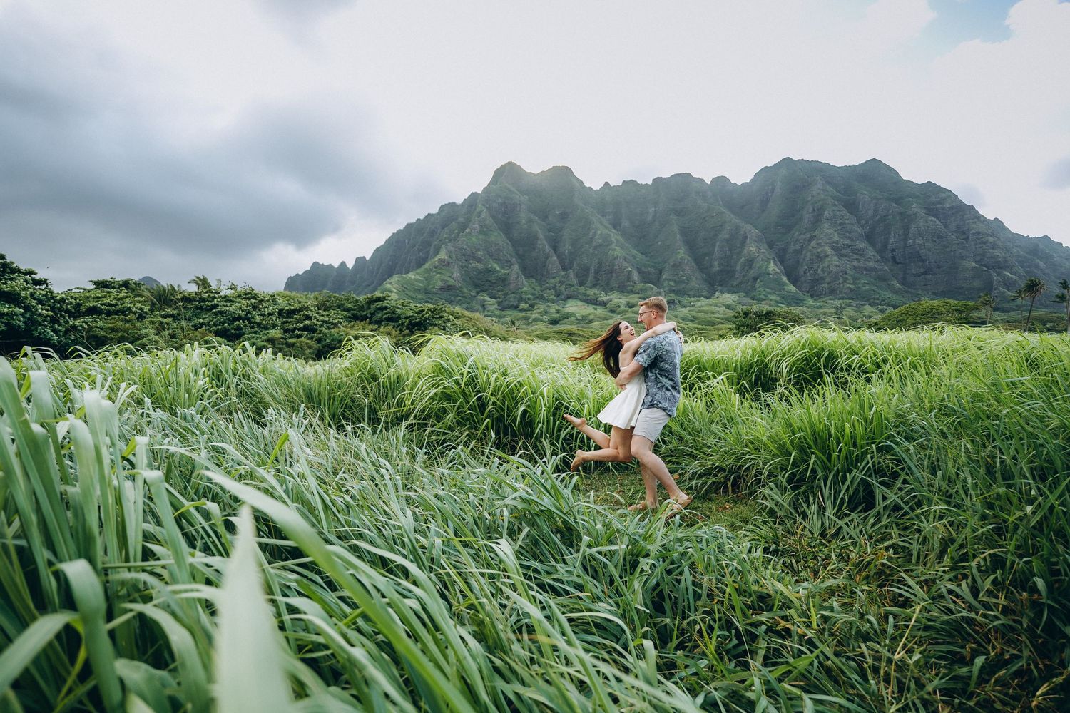 Couple playing in a lush green field under moody clouds, Kualoa Ranch couples photographer, Oahu, Hawaii
