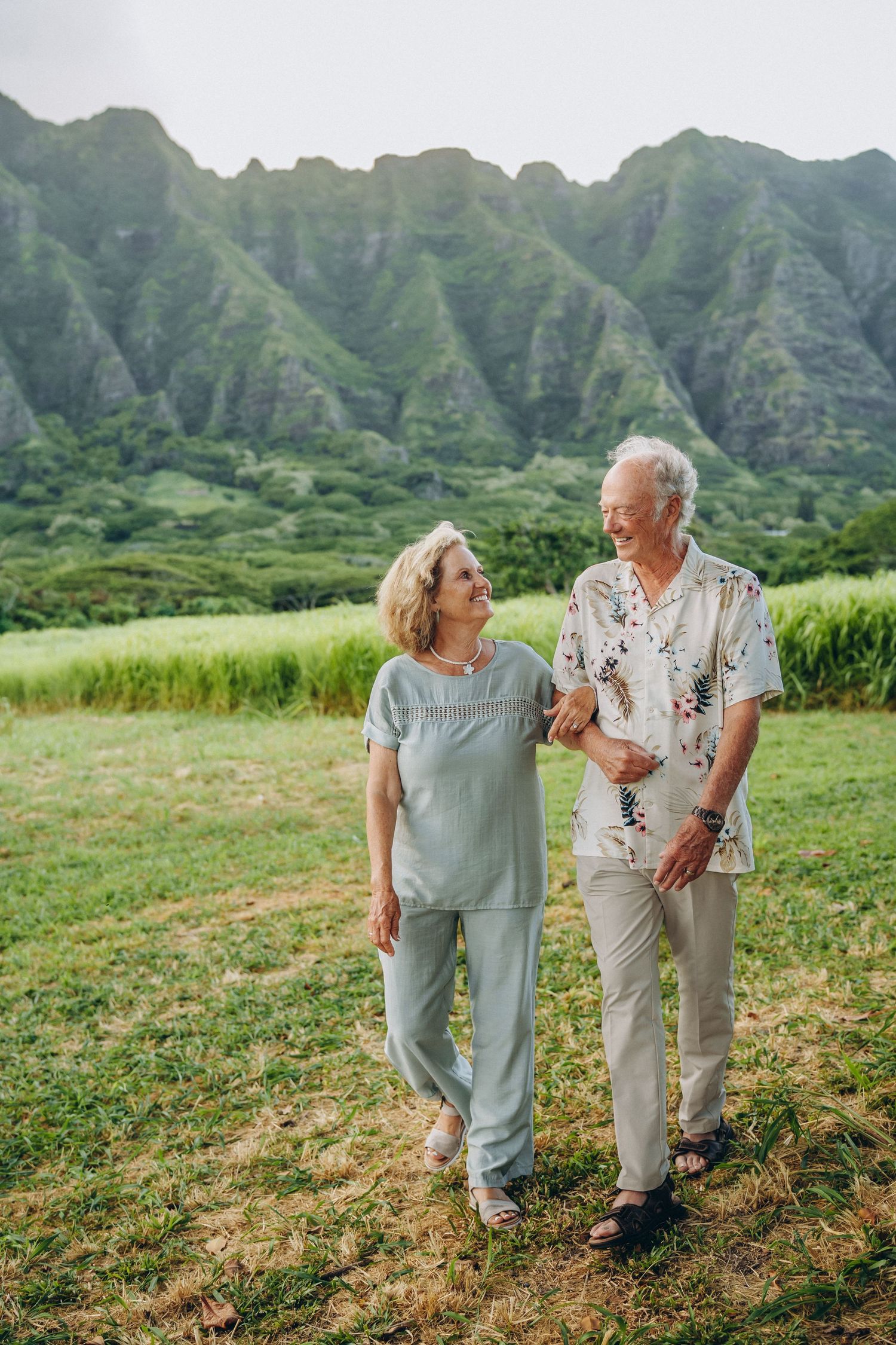 Grandparents walking together through a green field, Koʻolau mountains behind, Kualoa Ranch Oahu family photographer