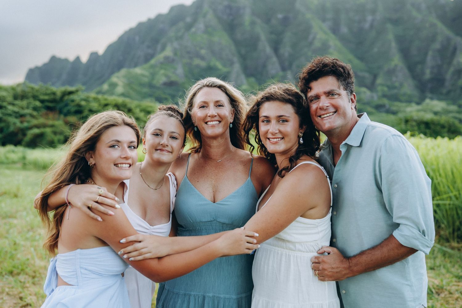 Family of five in a warm group hug in a green field, Koʻolau mountains behind, Kualoa Ranch Oahu family photographer