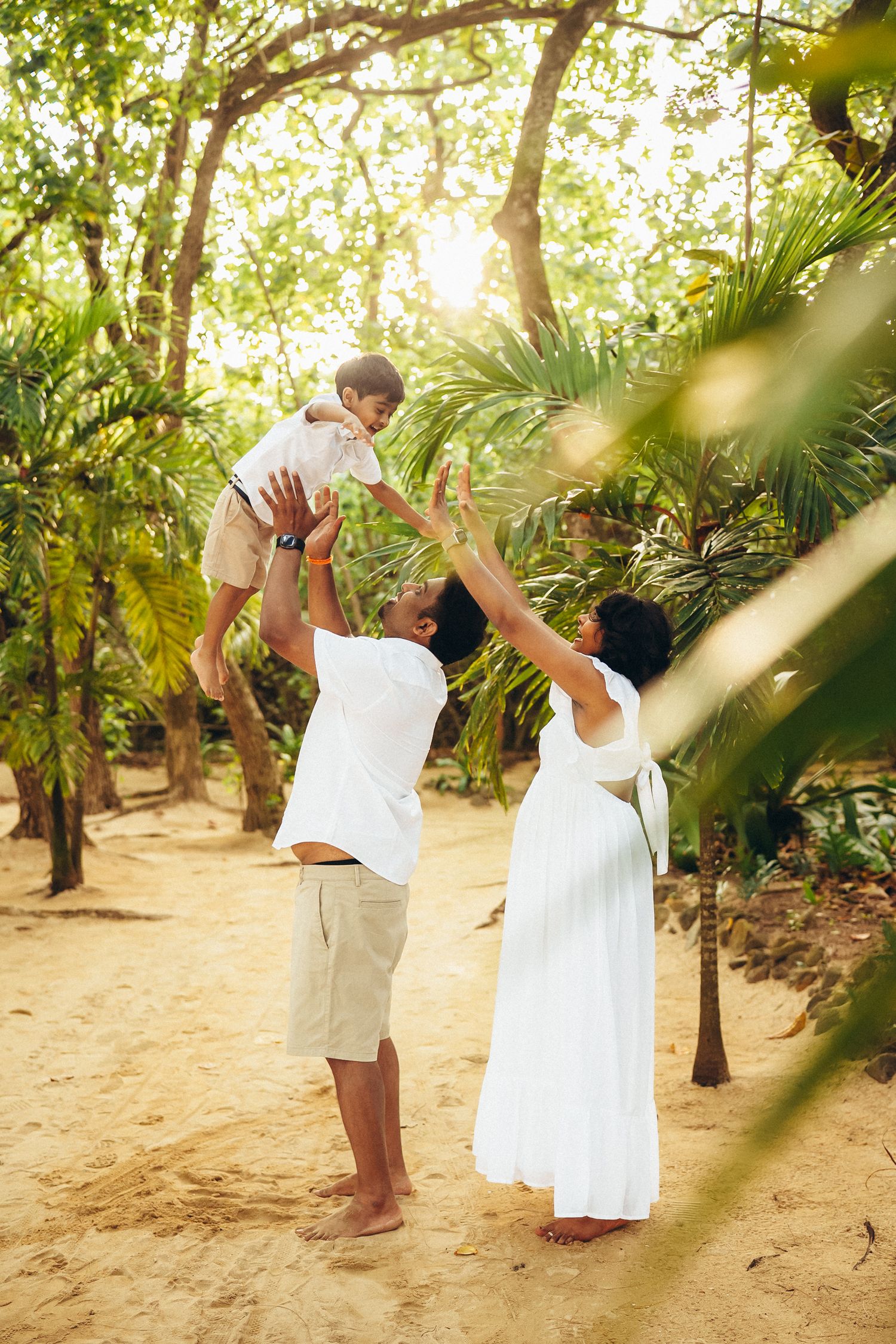 Joyful family photoshoot at Kualoa Ranch area, Secret Beach. Dad lifting kid up in the sun. Authentic Oahu lifestyle photography.