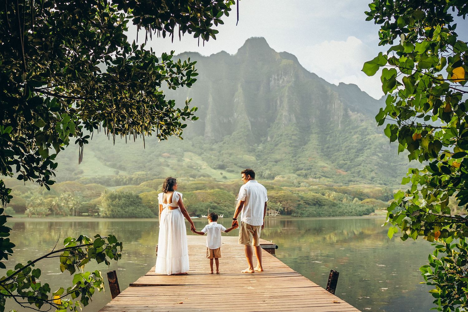 Family photoshoot at Kualoa Ranch, Oahu. A family standing on a wooden pier with majestic mountains in the background. Secret Beach vibes.