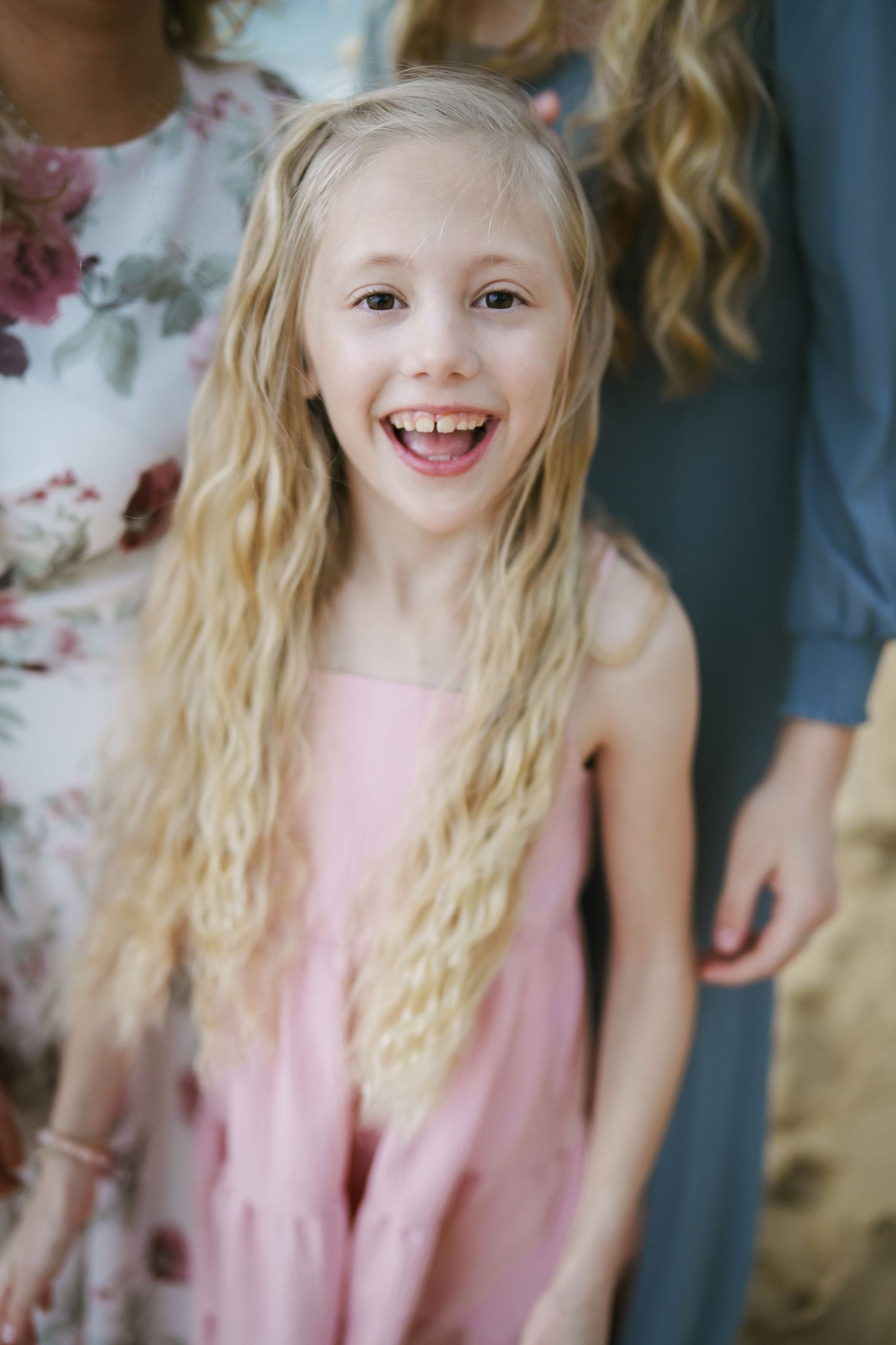 A close-up portrait of a blonde girl in a pink dress smiling at Ka’a’awa Beach, Oahu. A natural and bright moment captured at sunrise.