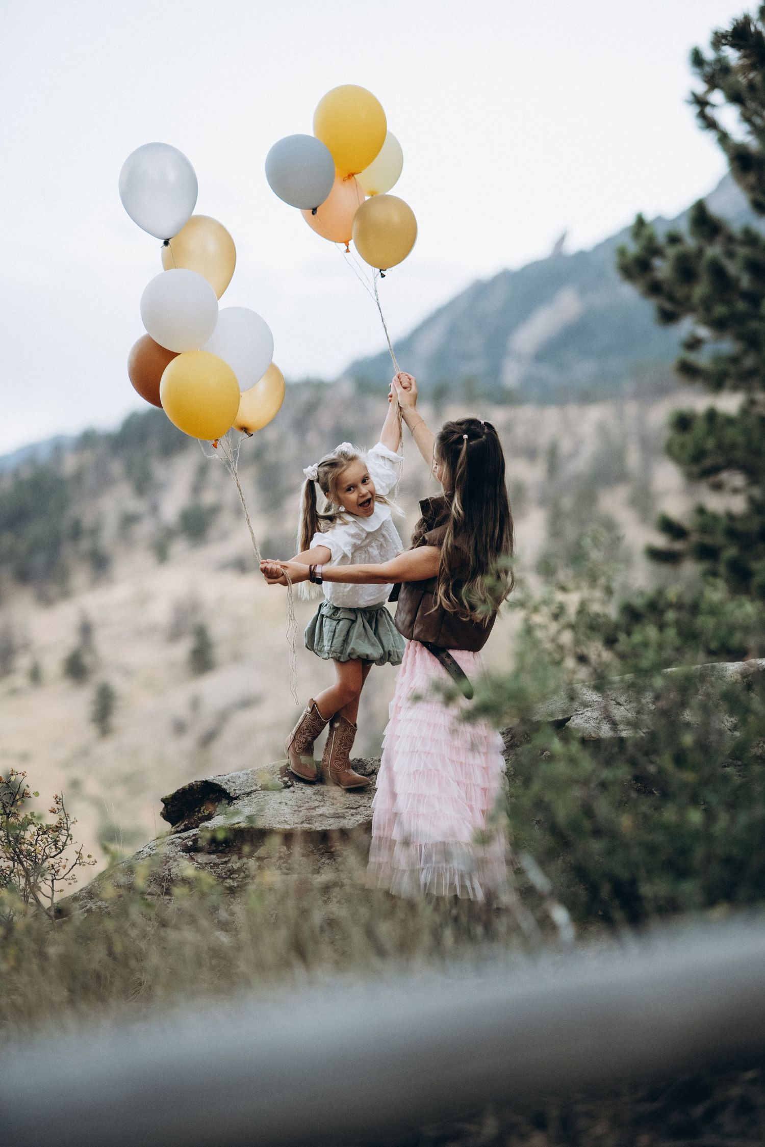 Mom lifting her daughter with balloons on a rocky hillside, Flatirons behind, Boulder family photographer at NCAR