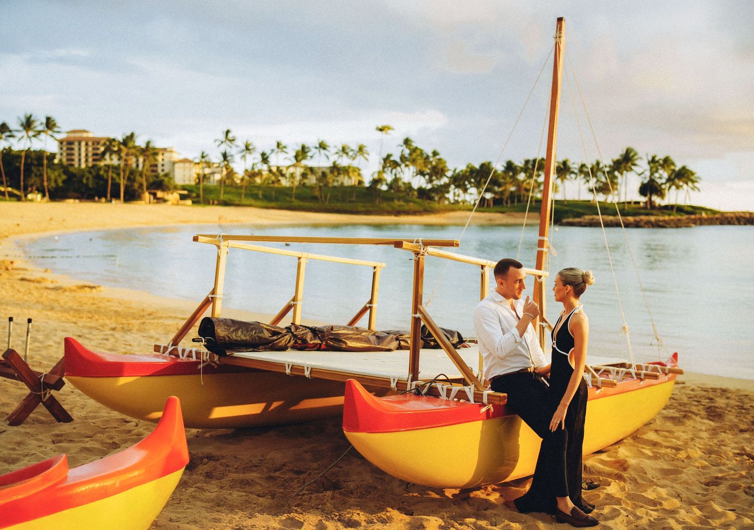 Colorful outrigger canoes line up along a sandy Hawaiian beach at sunset with palm trees in the background oahu engagement session on oahu
