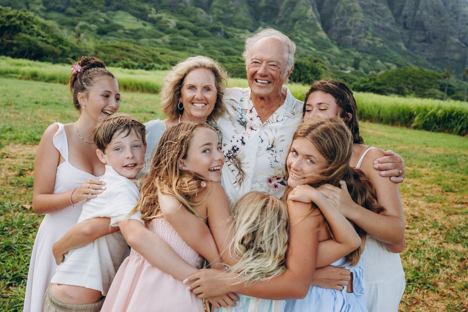 Multi-generational family hugging close with grandparents in a green field, Kualoa Ranch Oahu family photographer