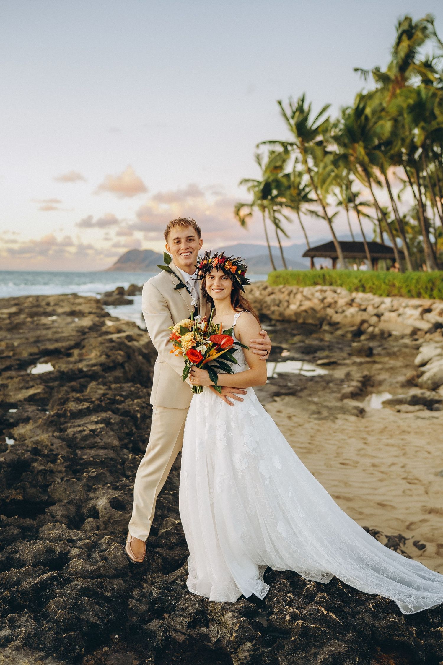 Full-length wedding portrait at Pohaku Point, Four Seasons Resort Oahu at Ko Olina. Bride and groom with palm trees and Pacific Ocean backdr