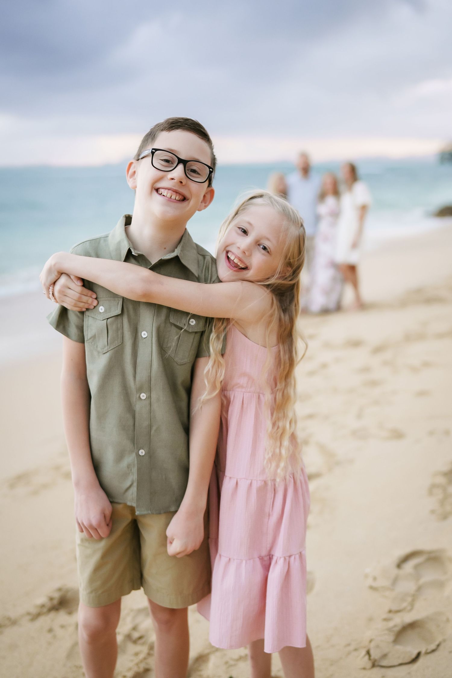 A heartwarming moment where a sister embraces her brother in the foreground, while the rest of the family stands behind them, watching with