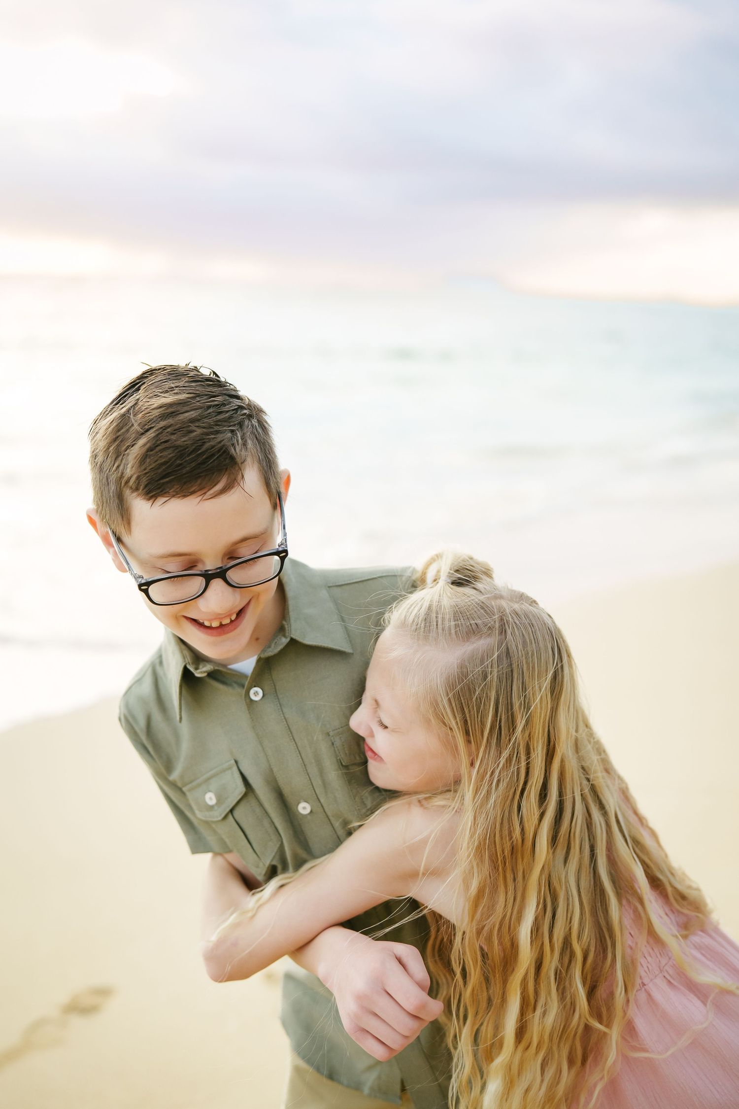 Sister hugging and laughing with her brother at Ka’a’awa Beach, Oahu. A sweet, candid sibling moment on the white sand at sunrise.