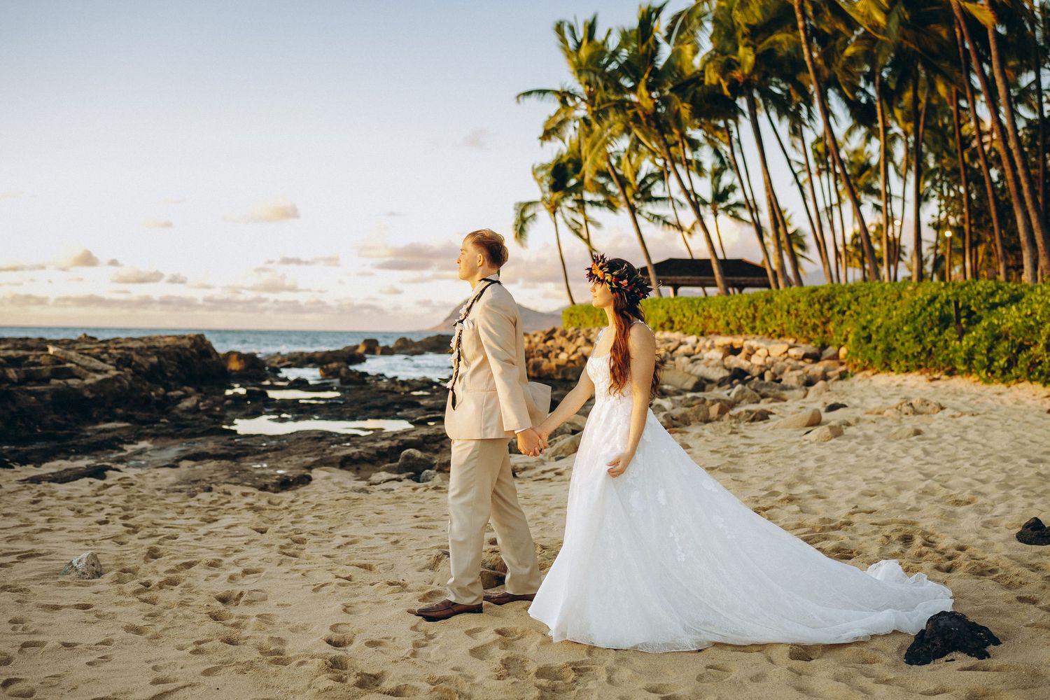 Full-length wedding portrait at Pohaku Point, Four Seasons Resort Oahu at Ko Olina. Bride and groom with palm trees and Pacific Ocean backdr
