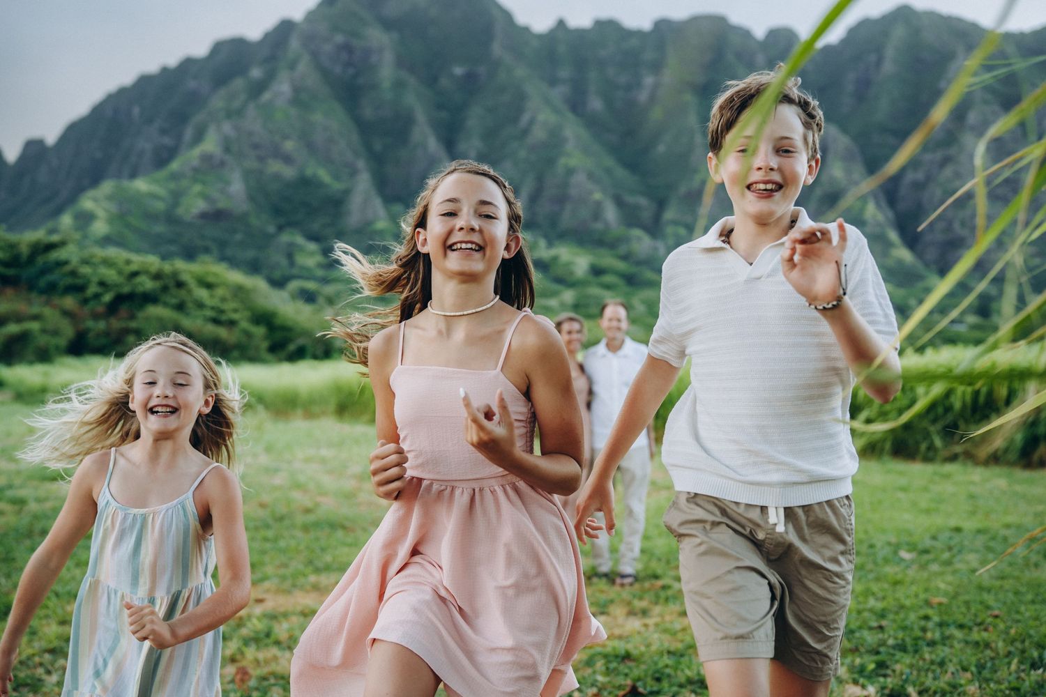 Kids running and laughing toward the camera in a green field, Kualoa Ranch Oahu family photographer, Hawaii