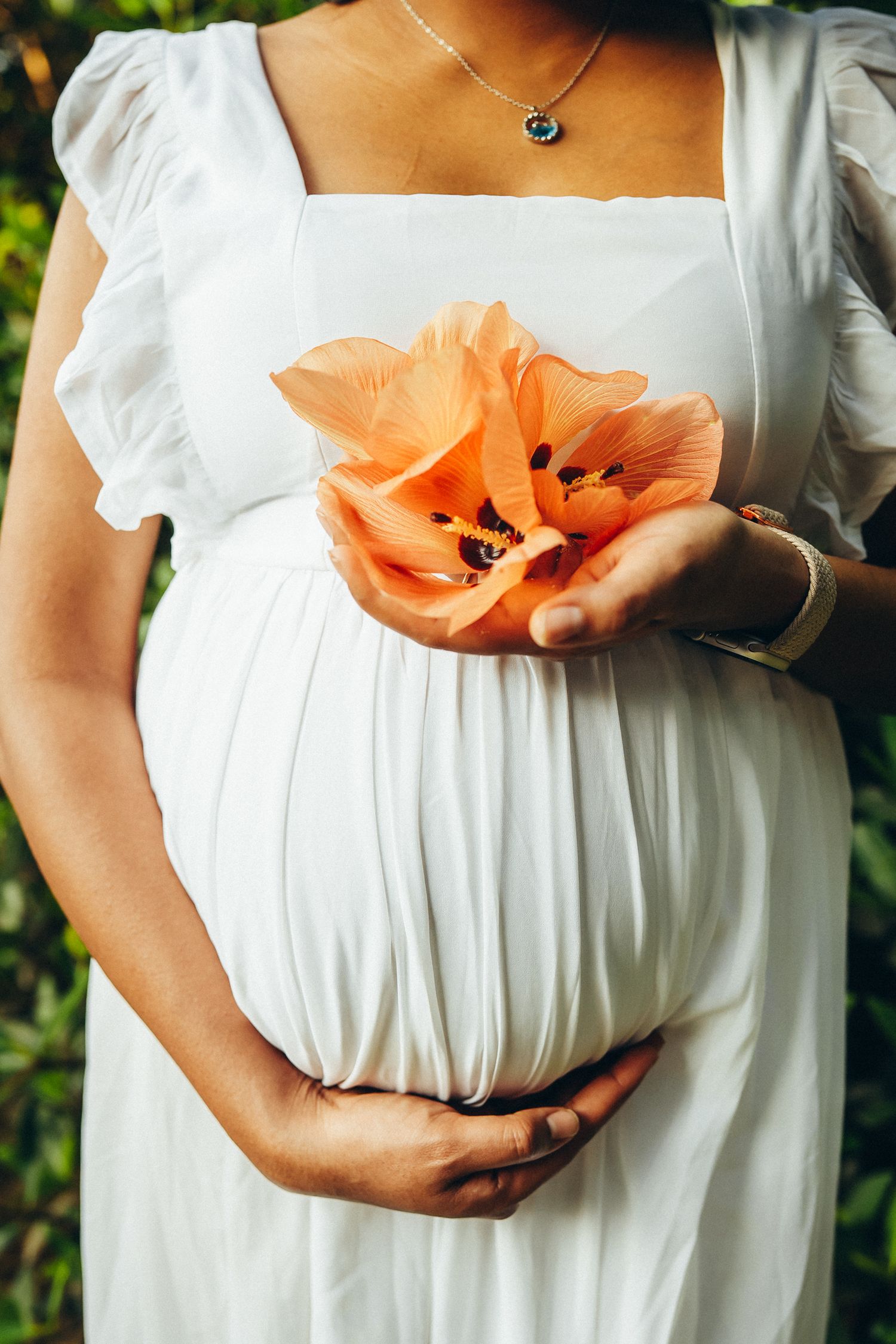 Maternity family photoshoot at Secret Beach. Close-up of a pregnant woman holding a tropical flower near Kualoa Ranch, Oahu.