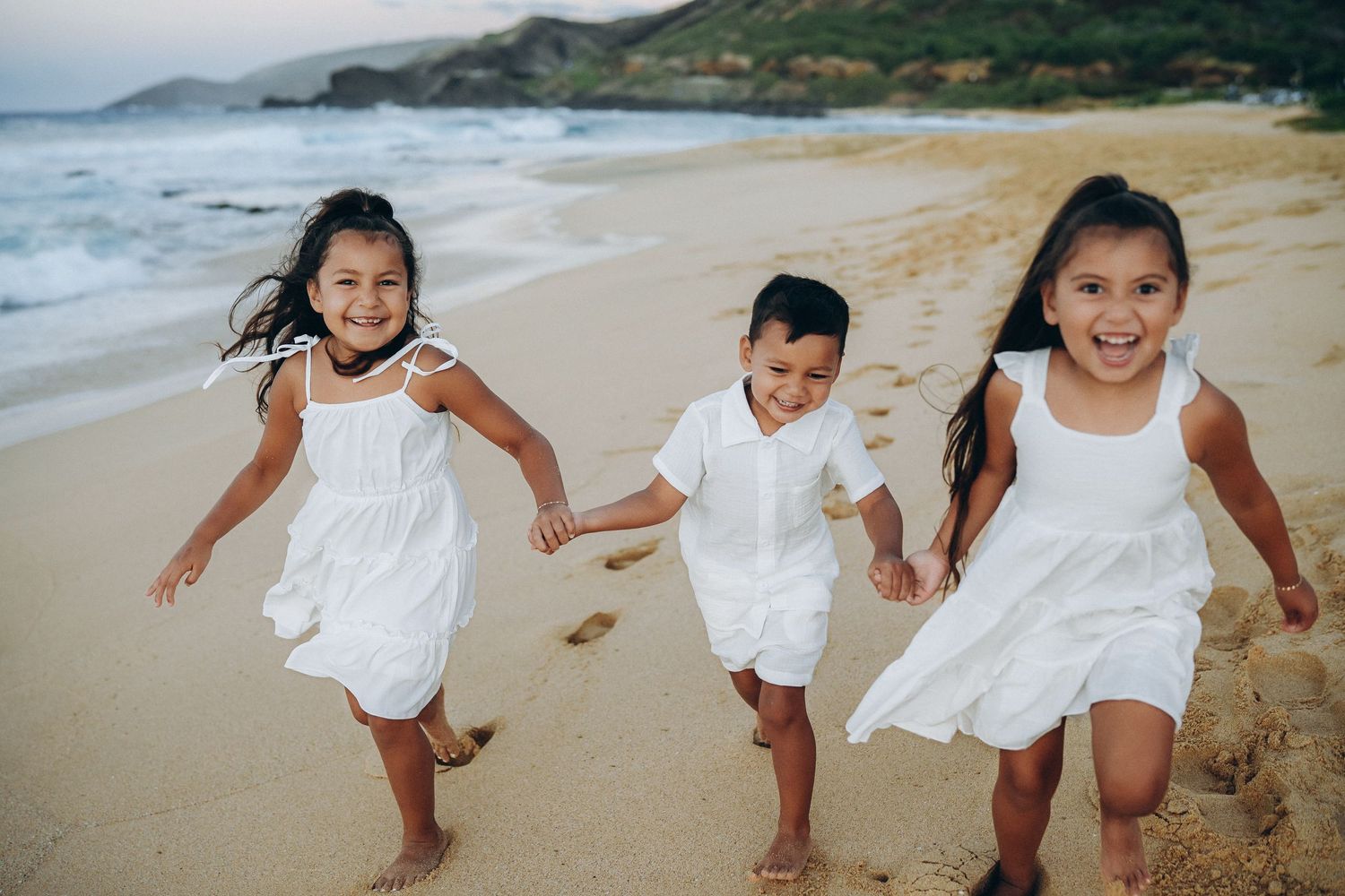 Three children in white running hand in hand along Sandy Beach, Oahu family photographer, Hawaii beach session
