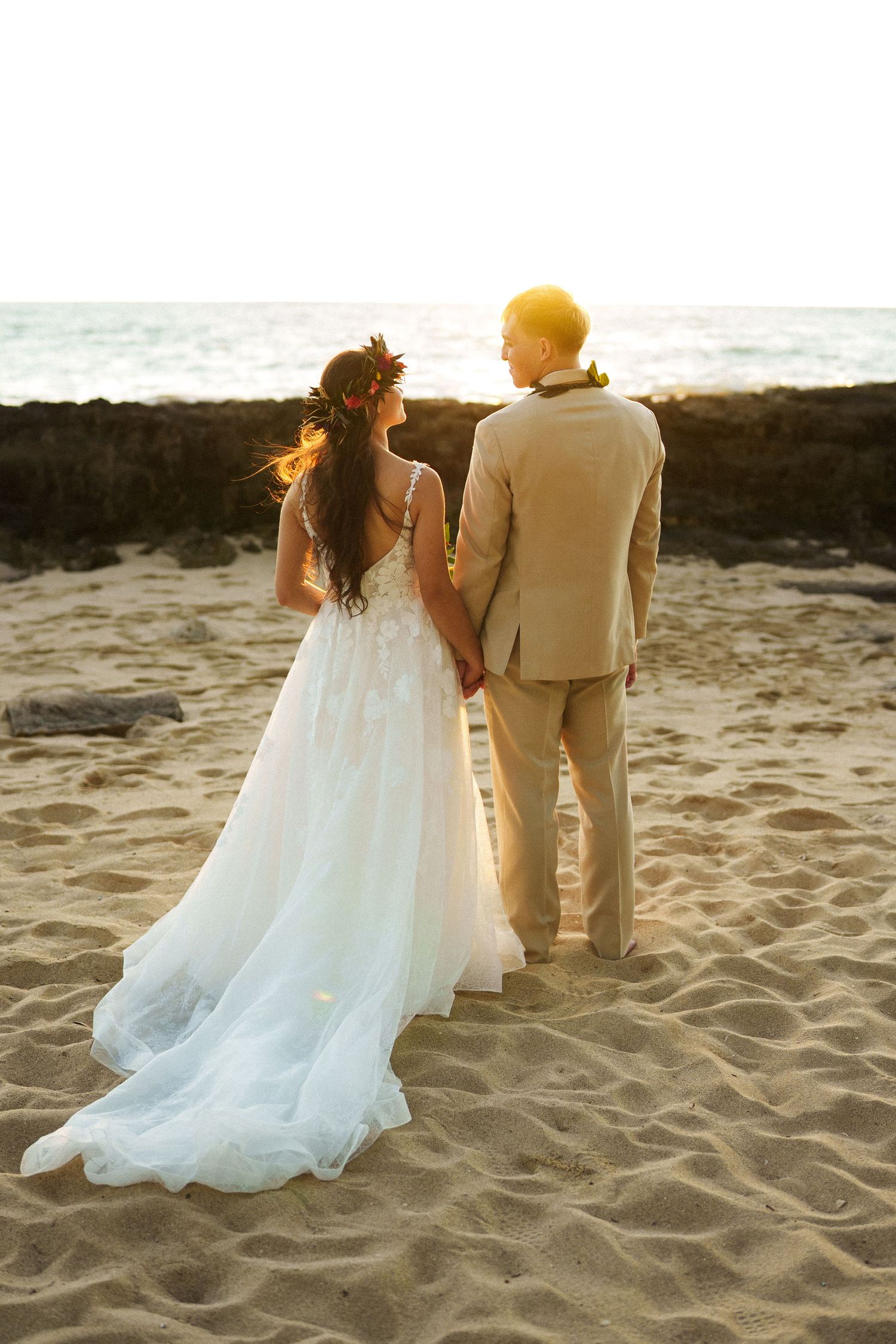 A stunning back-view of the newlyweds strolling along the sandy shores of Ko Olina. The contrast between the bride’s flowing white gown and