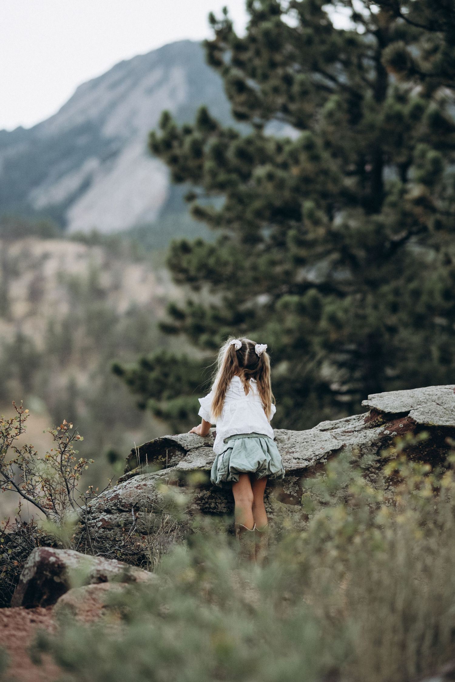 Little girl seen from behind sitting on rocks overlooking the Flatirons, Boulder family photographer at NCAR, Colorado