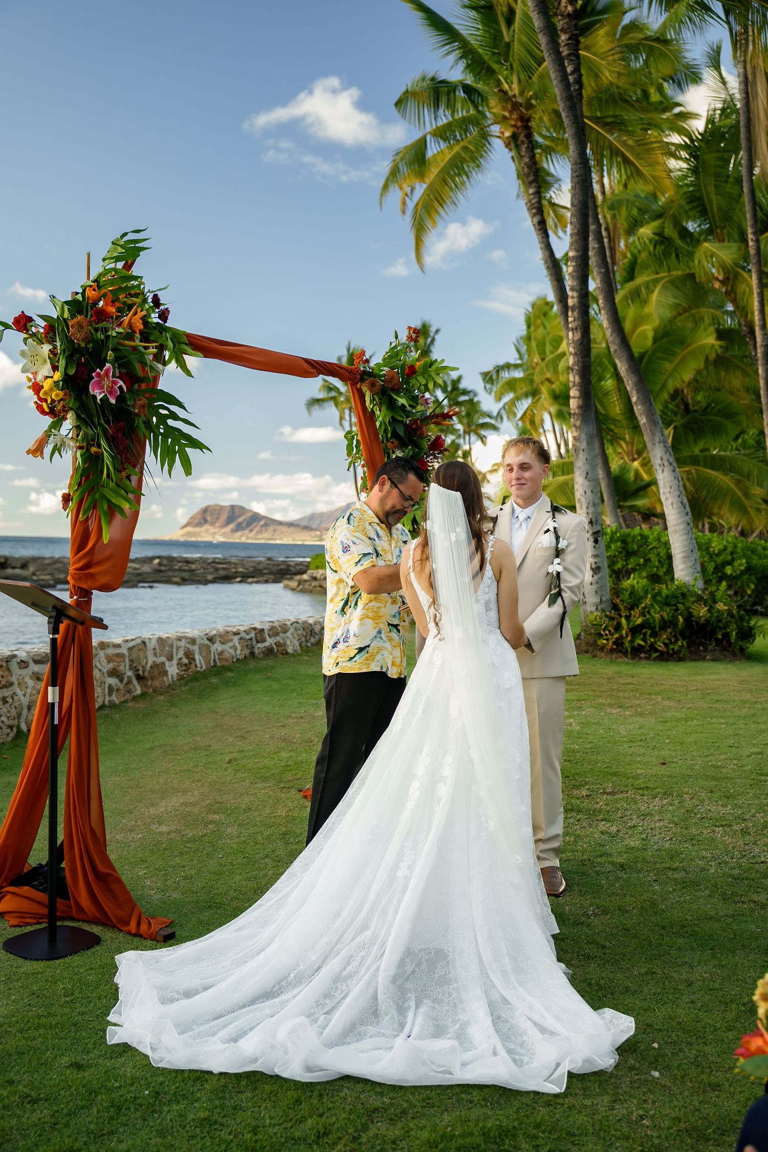 Bride & groom at a tropical altar in Ko Olina. Elegant Oahu wedding ceremony with ocean views and a stunning white dress train.